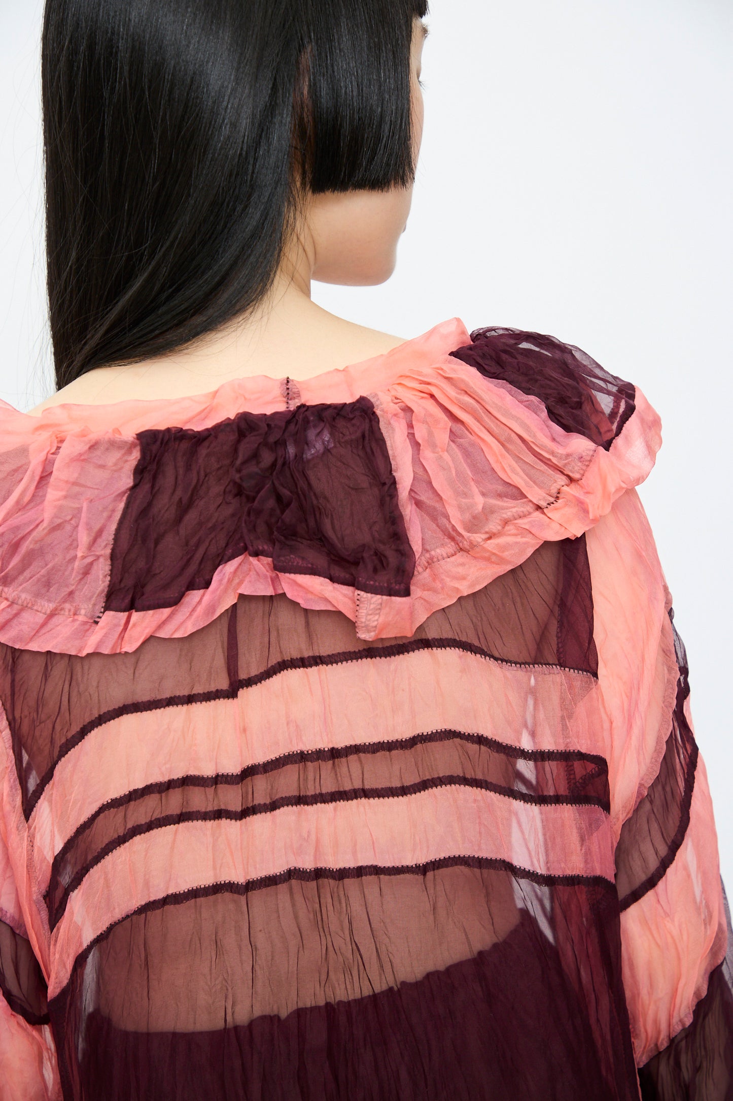 Back view of a long-haired individual wearing the SC103 Silk Organza Ides Dress in Venus, featuring pink and burgundy horizontal stripes with an oversized fit.
