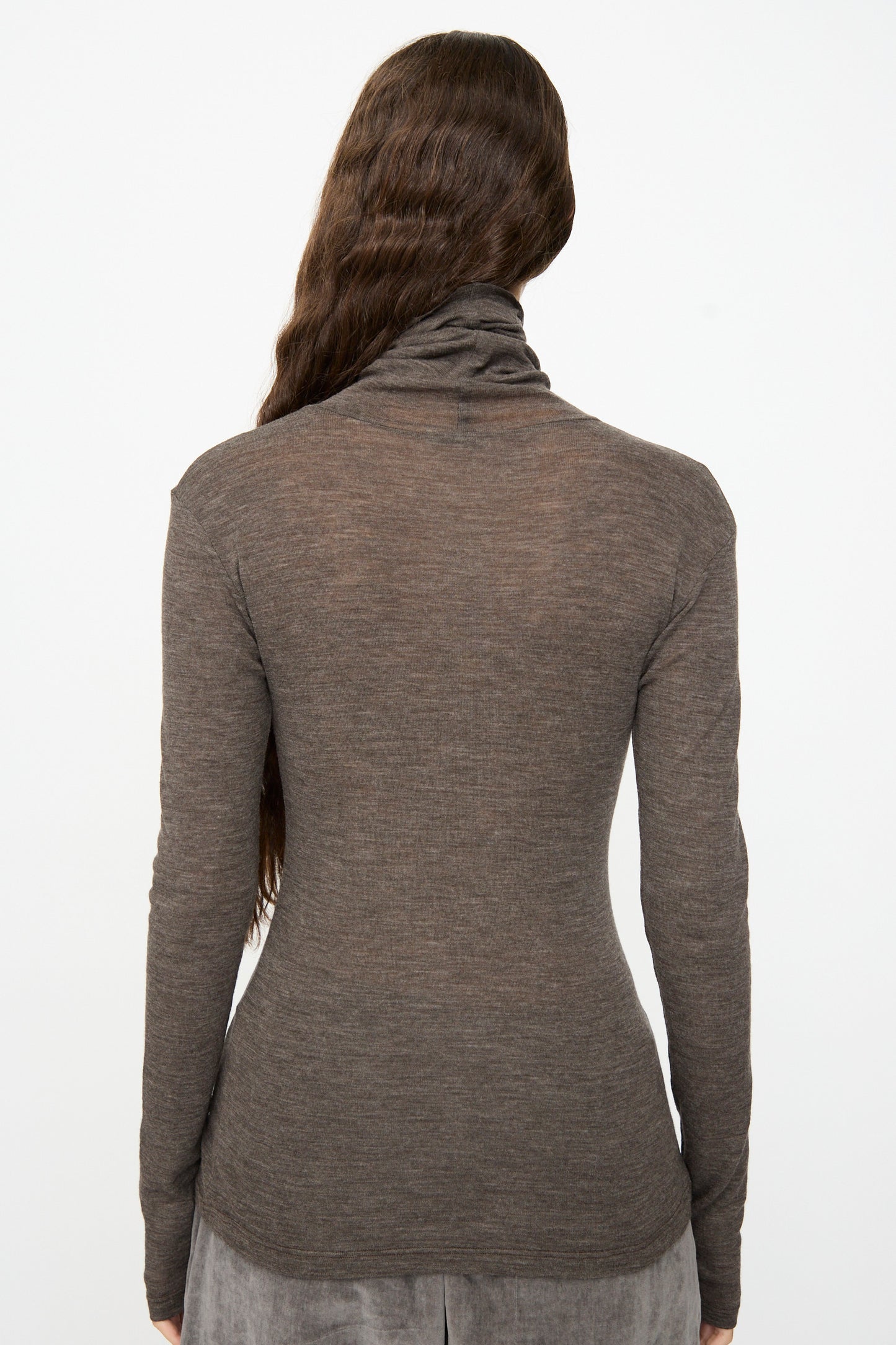 A person with long wavy brown hair is shown from the back against a plain white background, wearing the SONO Roberta Rollneck in Charcoal, a slim fit rolled turtleneck sweater.