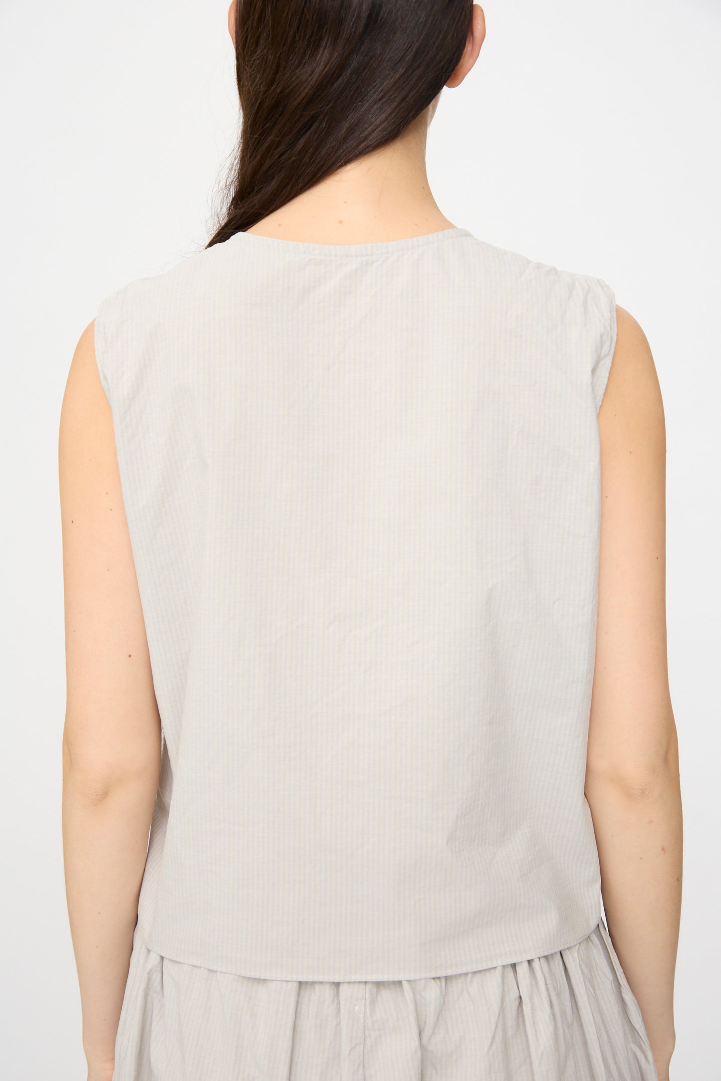 A woman with long brown hair is shown from the back wearing the SONO Victor Vest in Dusty Stripe Fine, paired with a matching skirt, against a plain white background.