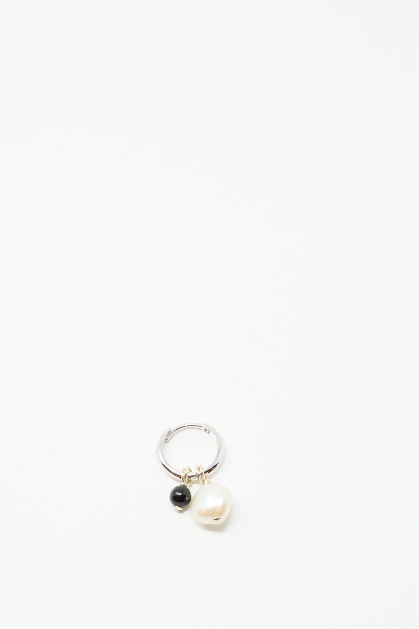 The Santangelo Baba Earring in Baby Black Agate features two dangling charms—a black agate bead and a white pearl— displayed on a plain white background.