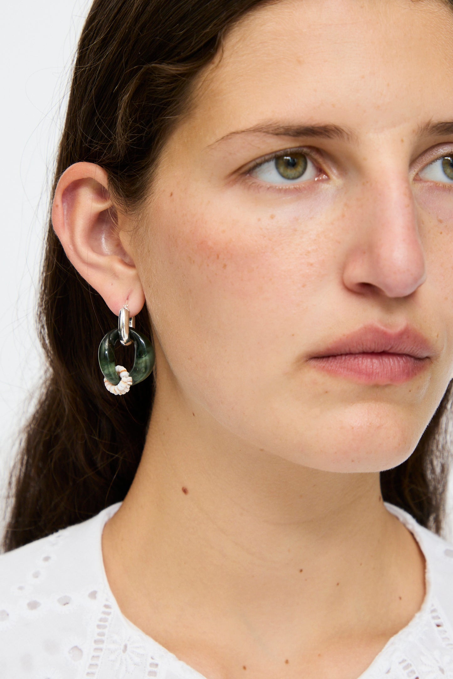 A woman with long brown hair wears a white eyelet top and Santangelo's Bad Orb Earrings in Jade, featuring large green hoops with a small white accent.