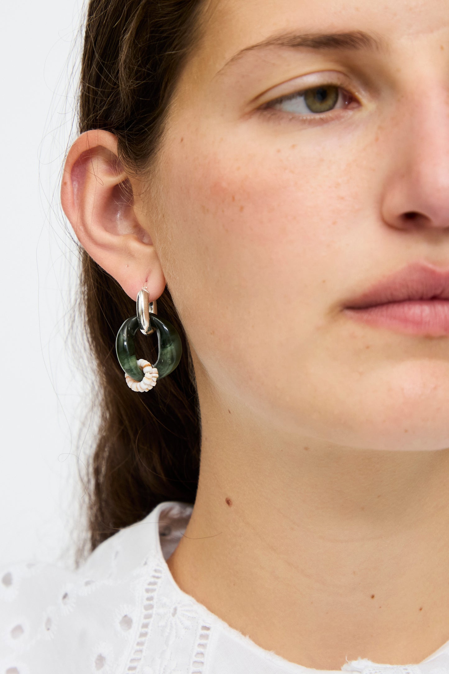 Close-up of a woman's face wearing a white eyelet top and Santangelo's Bad Orb Earrings in Jade—large circular sterling silver hoops adorned with green jade and white accents.