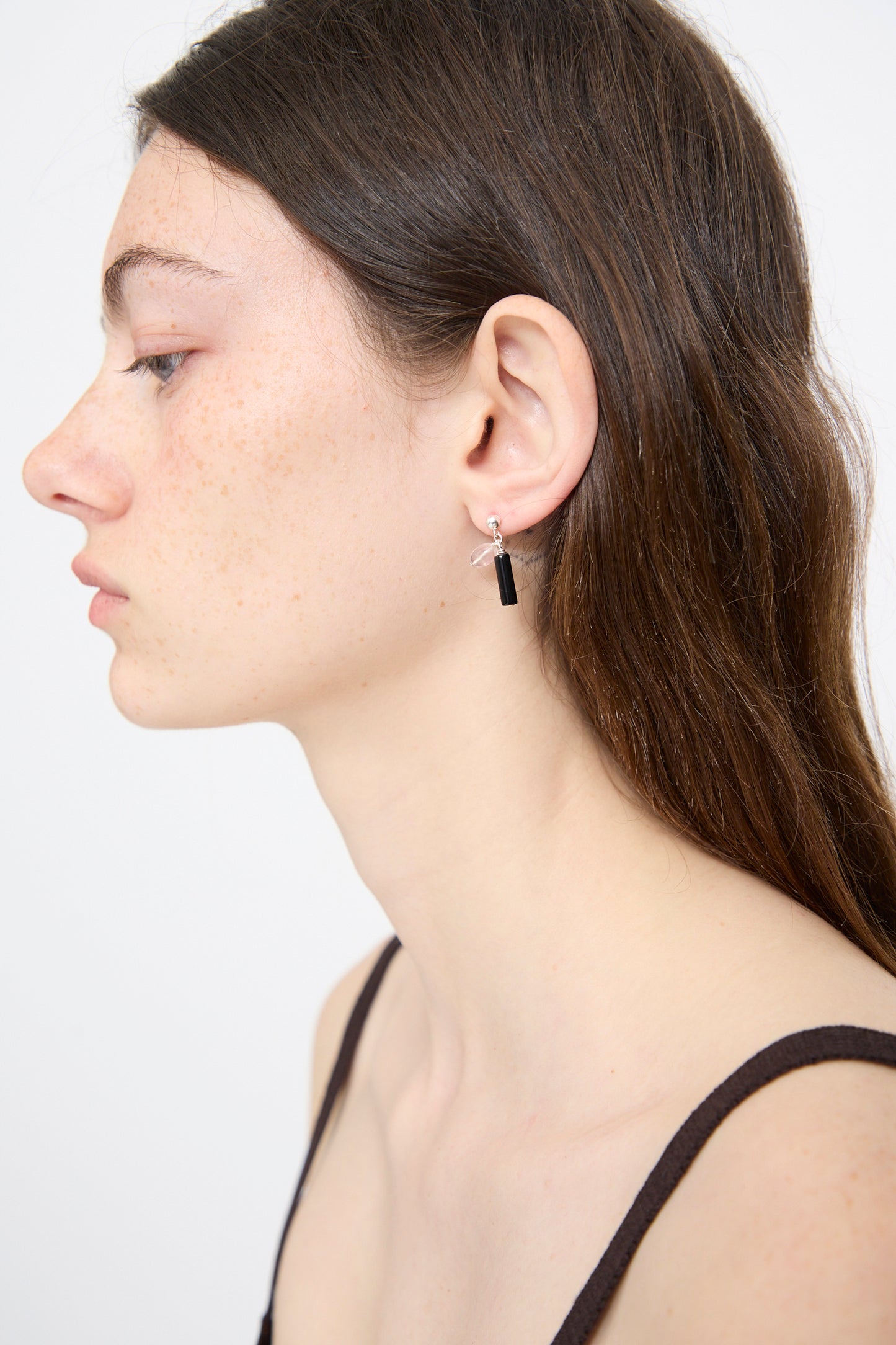 Woman with long brown hair wearing a black tank top and the Santangelo Bebecita Single Earring in Rose Quartz Onyx Drop, shown in profile against a plain background.