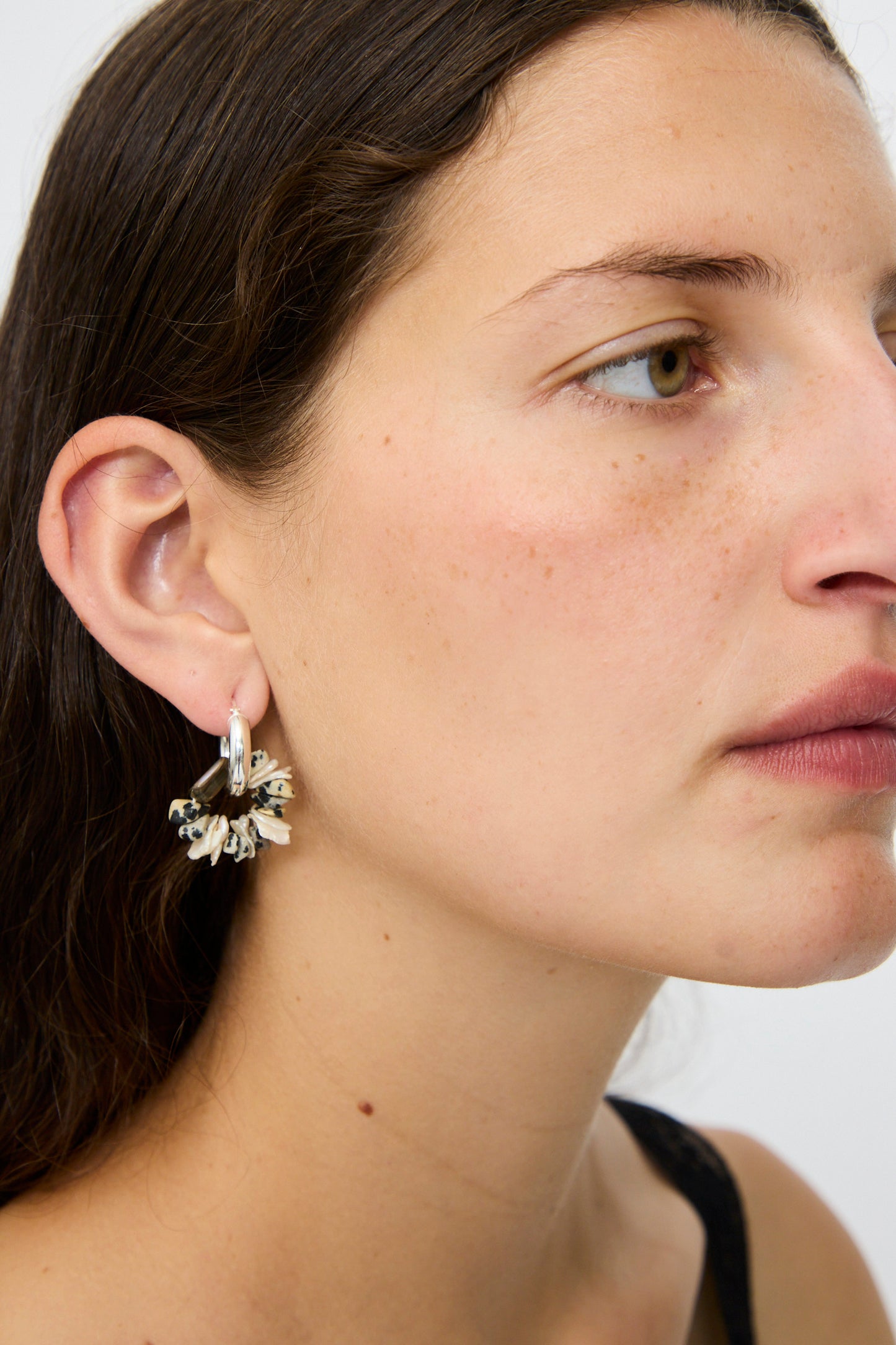A woman with long brown hair wears Santangelo's Che Bomba Earrings in Abalone Hoop in her left ear, shown in close-up side profile against a plain background.
