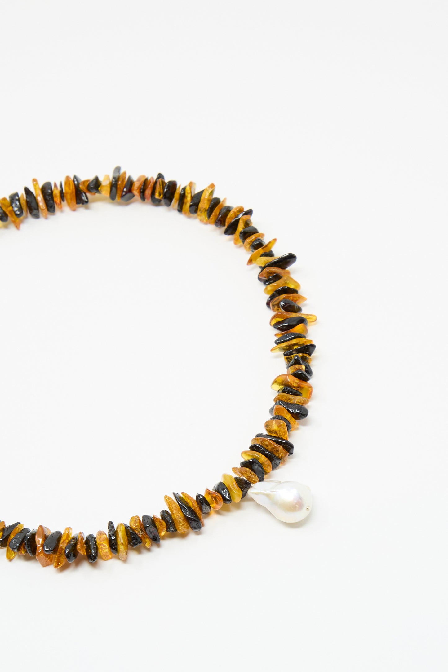 The Santangelo Kitano Necklace in Honey Stripe features irregular Baltic amber and black beads with a teardrop-shaped freshwater pearl pendant, showcased on a white background.