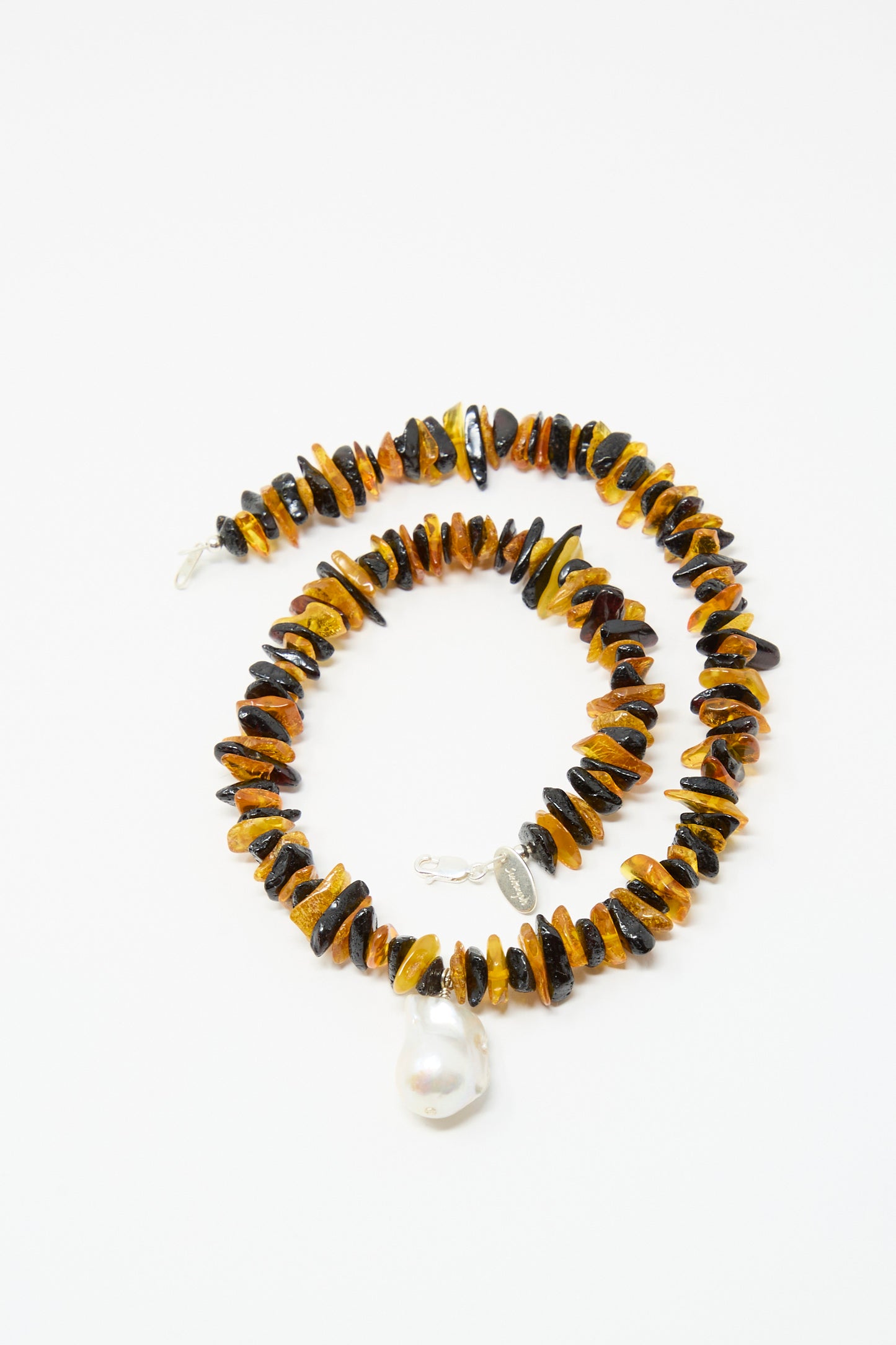The Kitano Necklace in Honey Stripe by Santangelo features alternating Baltic amber and dark brown beads, a large freshwater pearl pendant, and a sterling silver clasp, displayed on a white background.