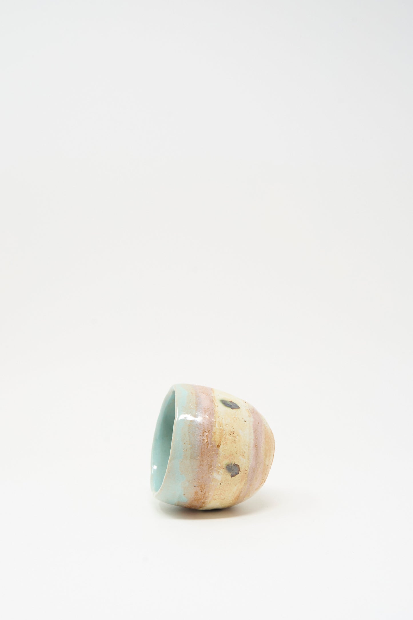 The Cup in Dots II by Shino Takeda is a small, hand-painted ceramic cup featuring a pastel glaze with brown spots, shown lying on its side against a plain white background.