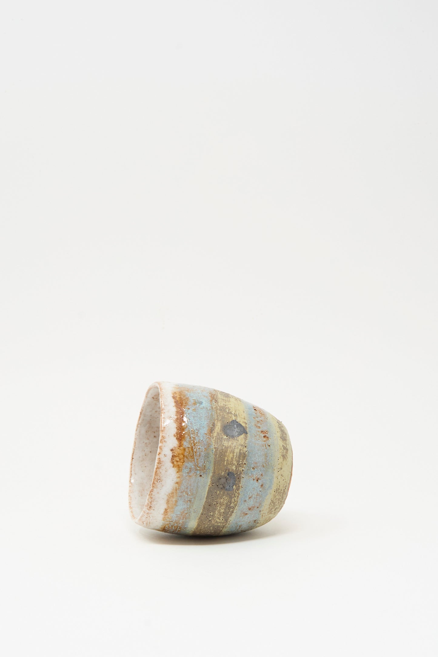 The Cup Tall in Dots I by Shino Takeda, a small hand-painted ceramic piece featuring dotted patterns, rests on its side against a plain white background.