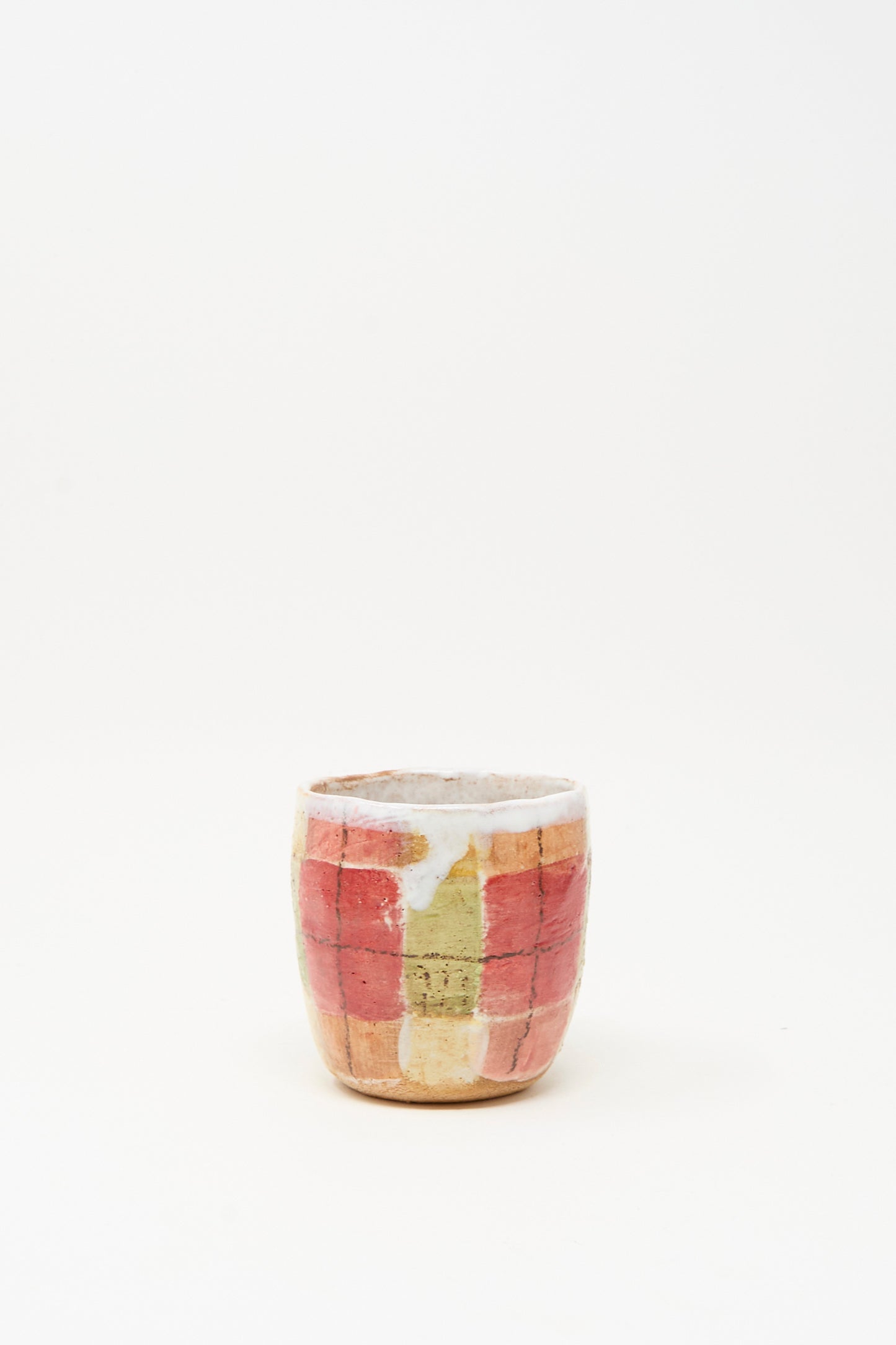 The "Cup in Red Plaid I" by Shino Takeda is a small, hand-painted ceramic cup with a red, yellow, and beige grid design on a plain white background.