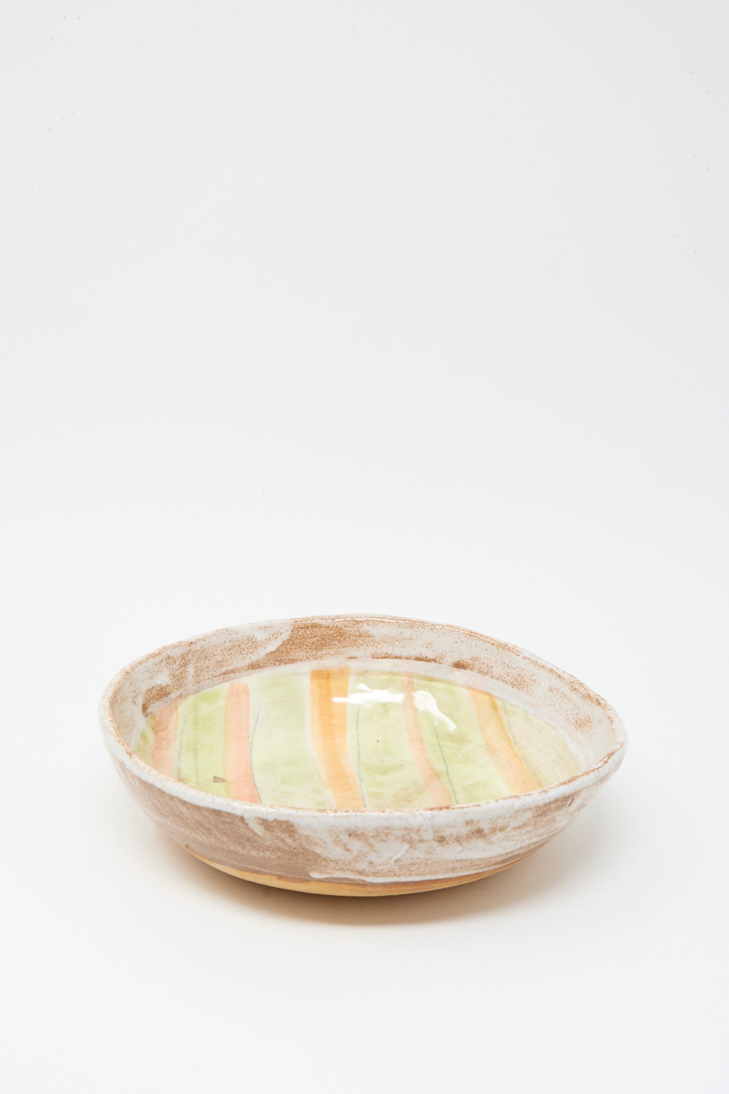 The Serving Bowl in Stripes by Shino Takeda is a handmade ceramic bowl with a textured earthy rim and glazed interior featuring vertical yellow and orange stripes.
