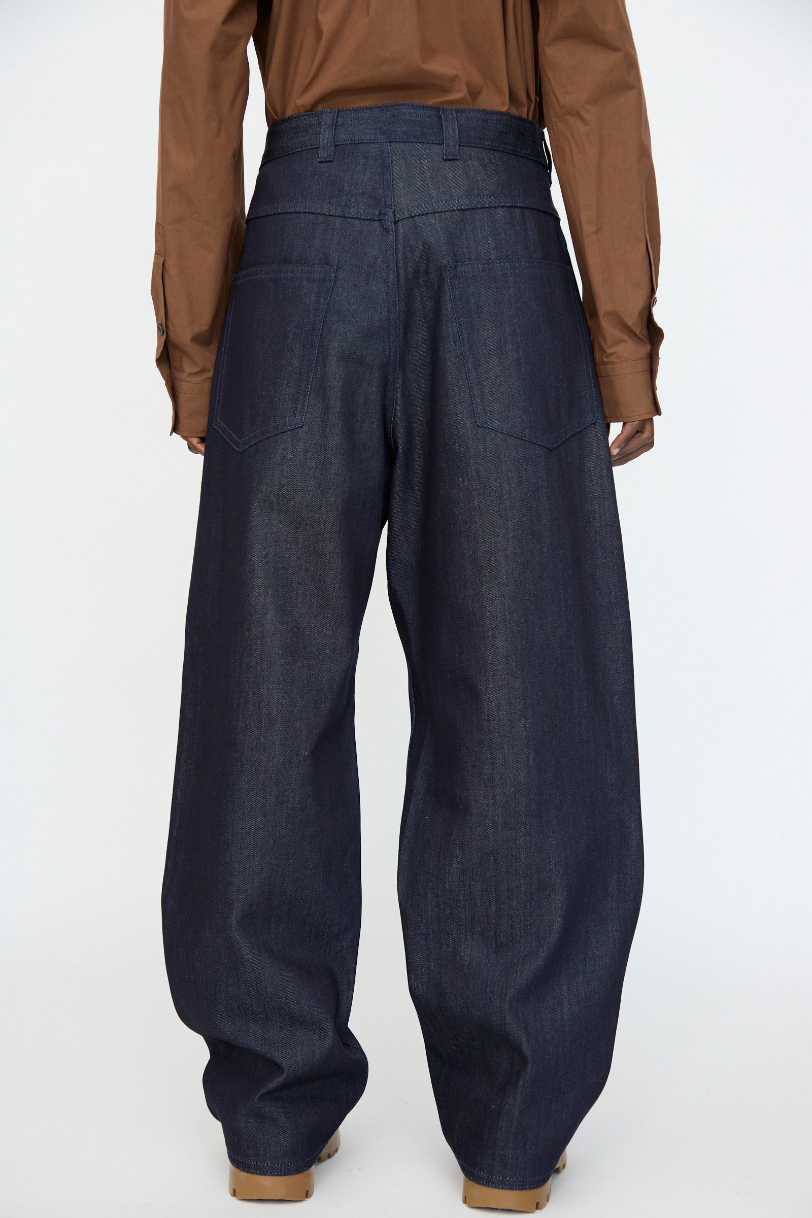 A person wearing the Sofie D'Hoore Denim Peggy Pant in Raw with a brown long-sleeve shirt, facing away from the camera against a plain background.