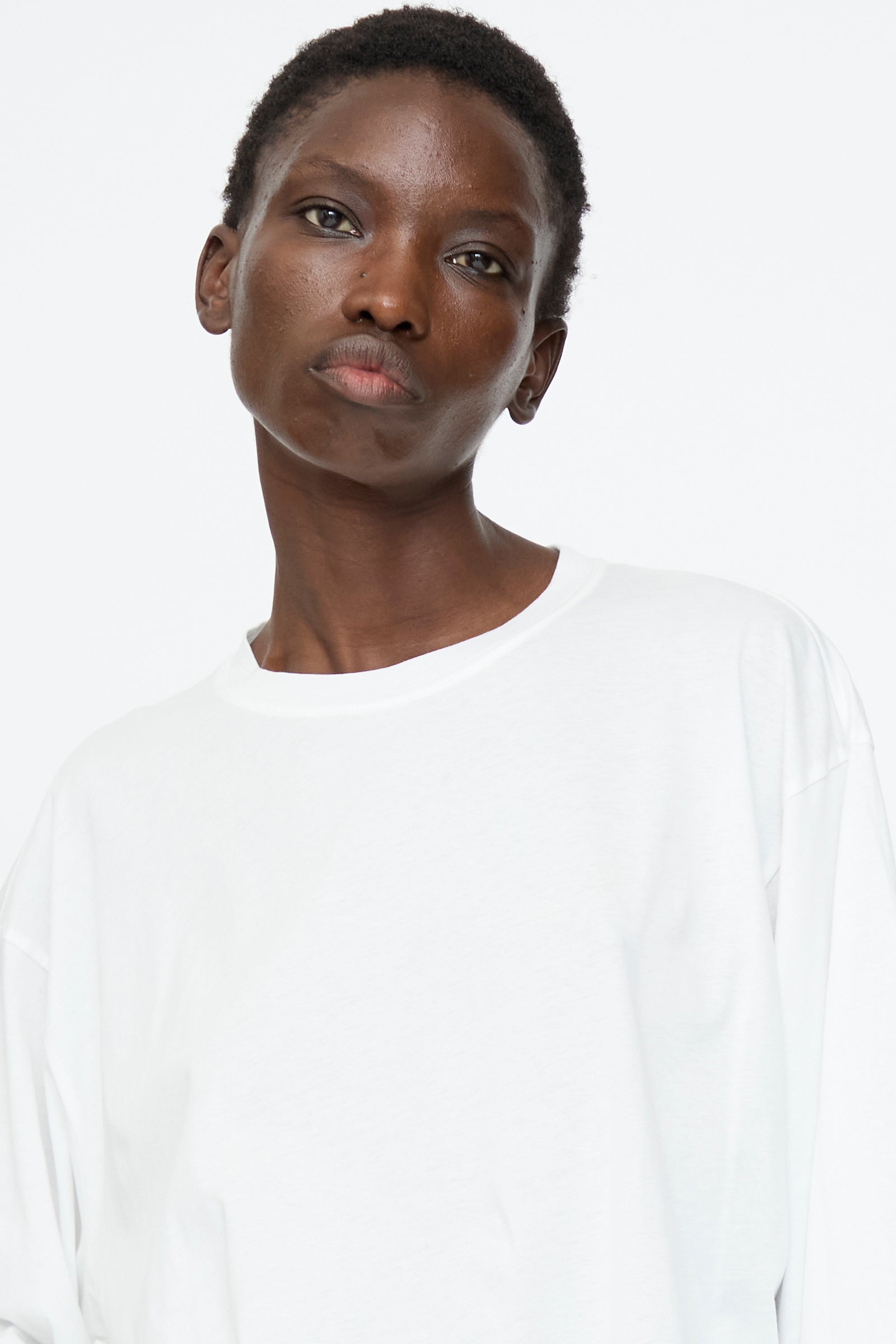A person with short hair wears the Sofie D'Hoore Fine Cotton Jersey Toledo Tee in Off White, featuring a relaxed fit and long sleeves, standing against a white background and looking directly at the camera with a neutral expression.