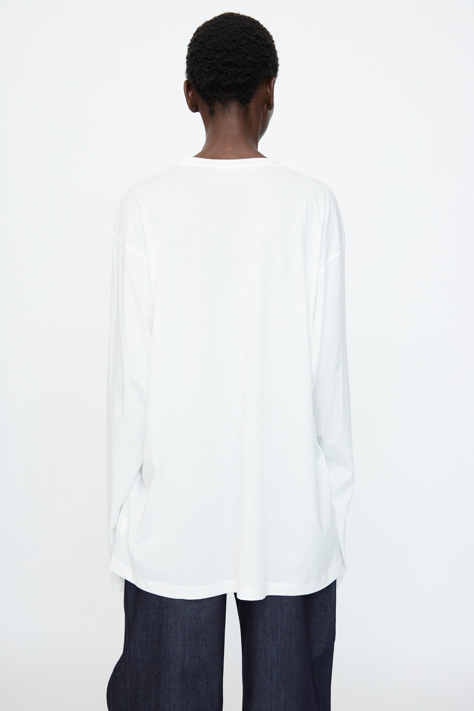 A person with short hair faces away, wearing the Sofie D'Hoore Fine Cotton Jersey Toledo Tee in Off White and dark pants, set against a plain white background.