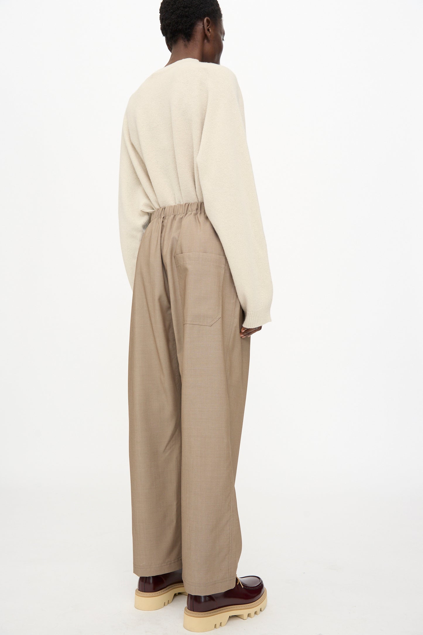 Person standing against a white background, wearing a cream sweater and Sofie D'Hoore Light Mohair Wool Pinot Pant in Quartz, styled with brown platform shoes.