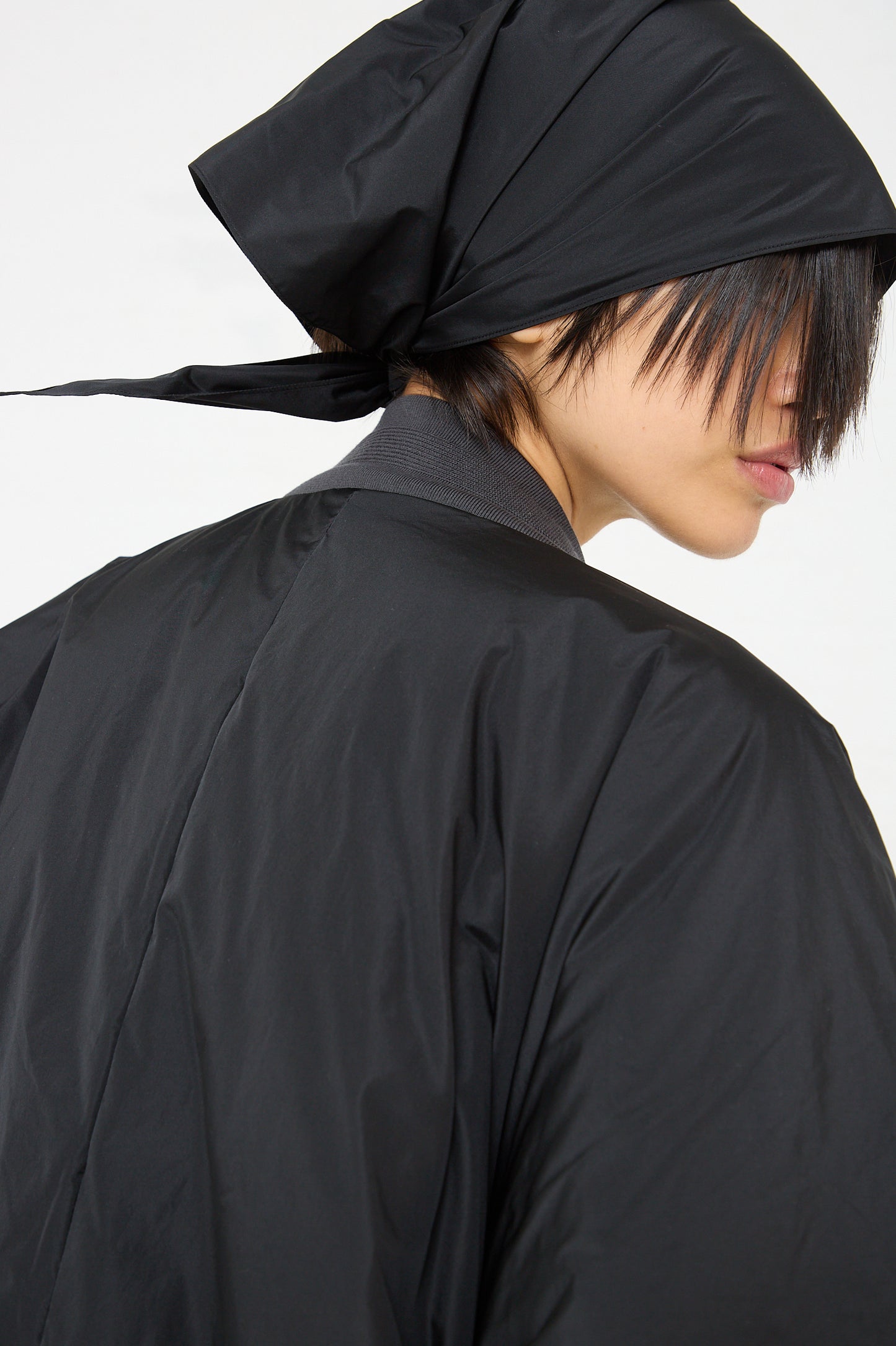 The back view of a woman wearing a black hooded coat with the Sofie D'Hoore Quilted Down Reversible Orion Bomber in Black and Nude.
