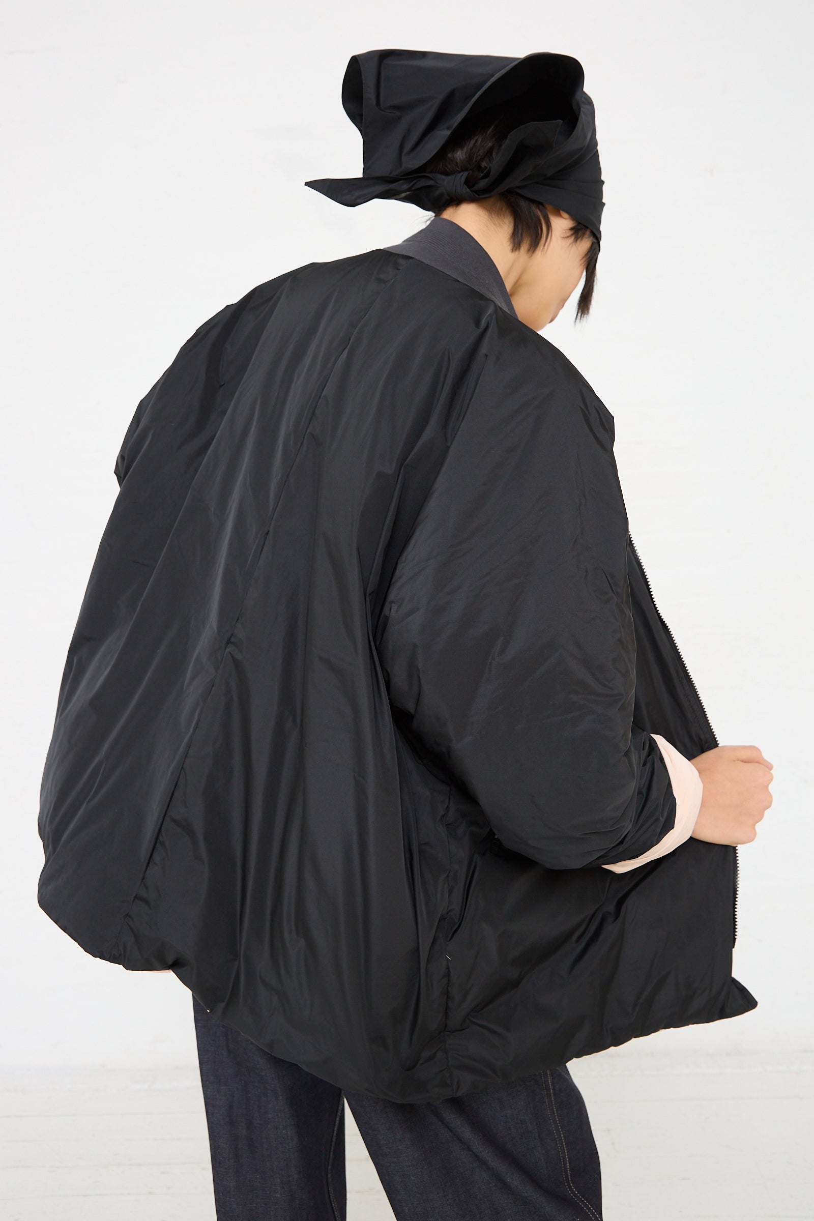The back of a woman wearing a Sofie D'Hoore Quilted Down Reversible Orion Bomber in Black and Nude with a ribbed band collar.
