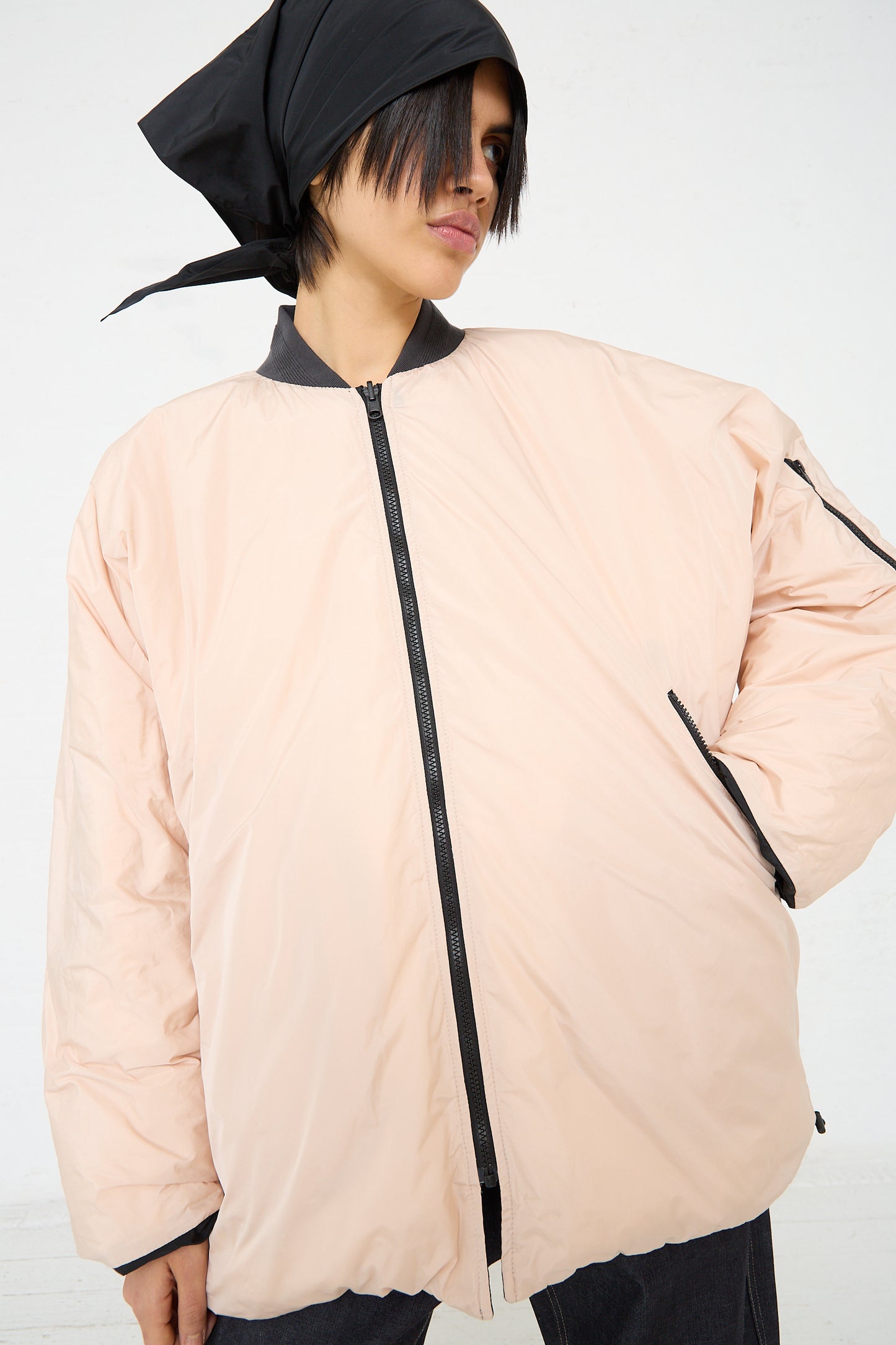 A woman wearing a pink Quilted Down Reversible Orion Bomber jacket by Sofie D'Hoore and a black hat.