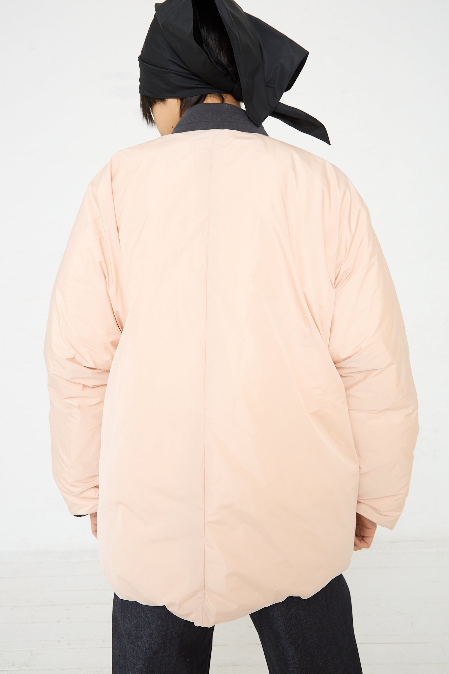 The back of a woman wearing a pink Sofie D'Hoore Quilted Down Reversible Orion Bomber in Black and Nude Bomber Jacket with a ribbed band collar.