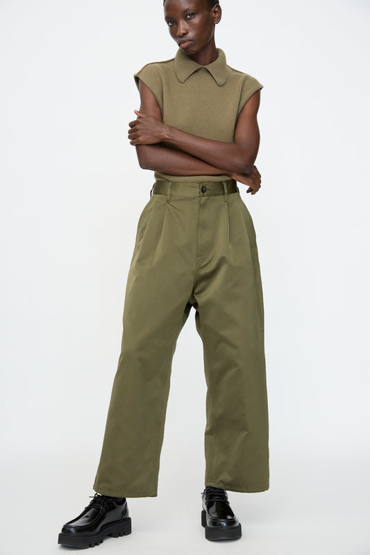 A person wears the Satin Polke Pant in Laurel by Sofie D'Hoore with a sleeveless olive top and black chunky shoes, standing against a plain white background.