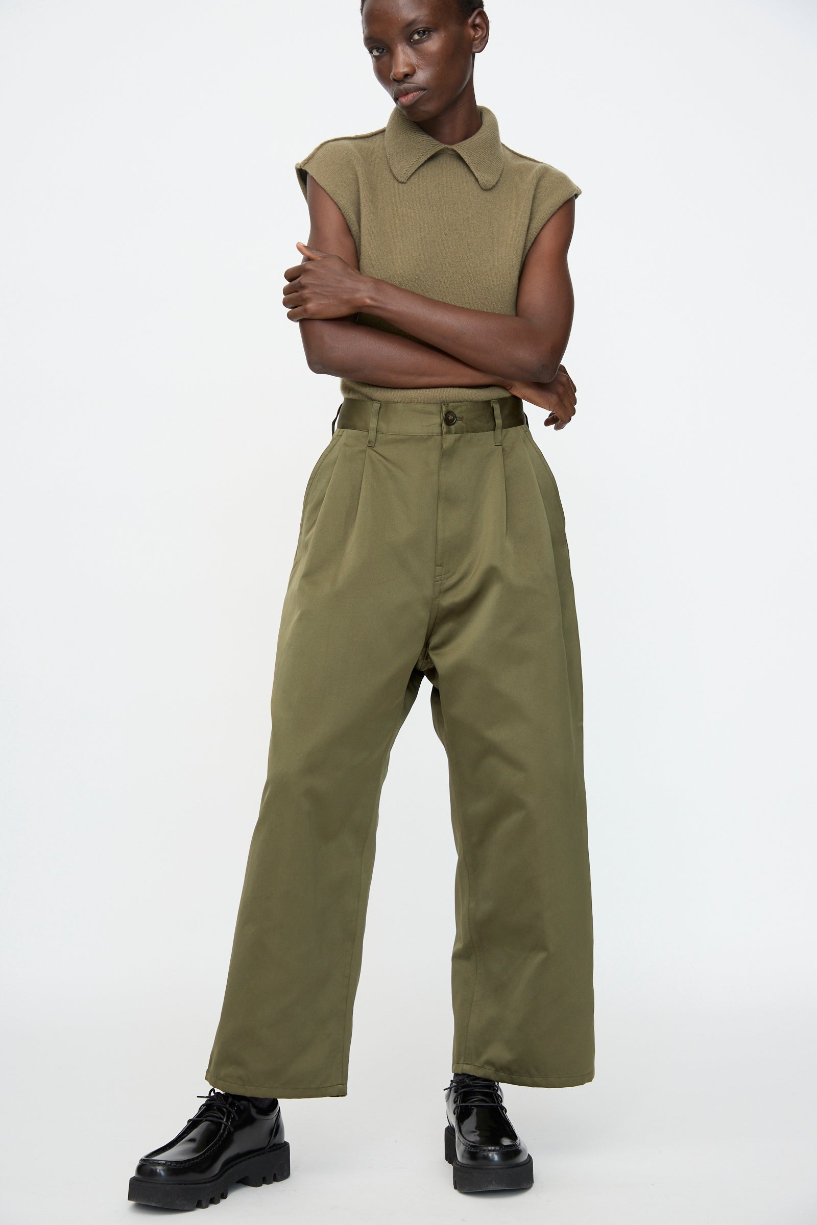 A person wears the Satin Polke Pant in Laurel by Sofie D'Hoore with a sleeveless olive top and black chunky shoes, standing against a plain white background.