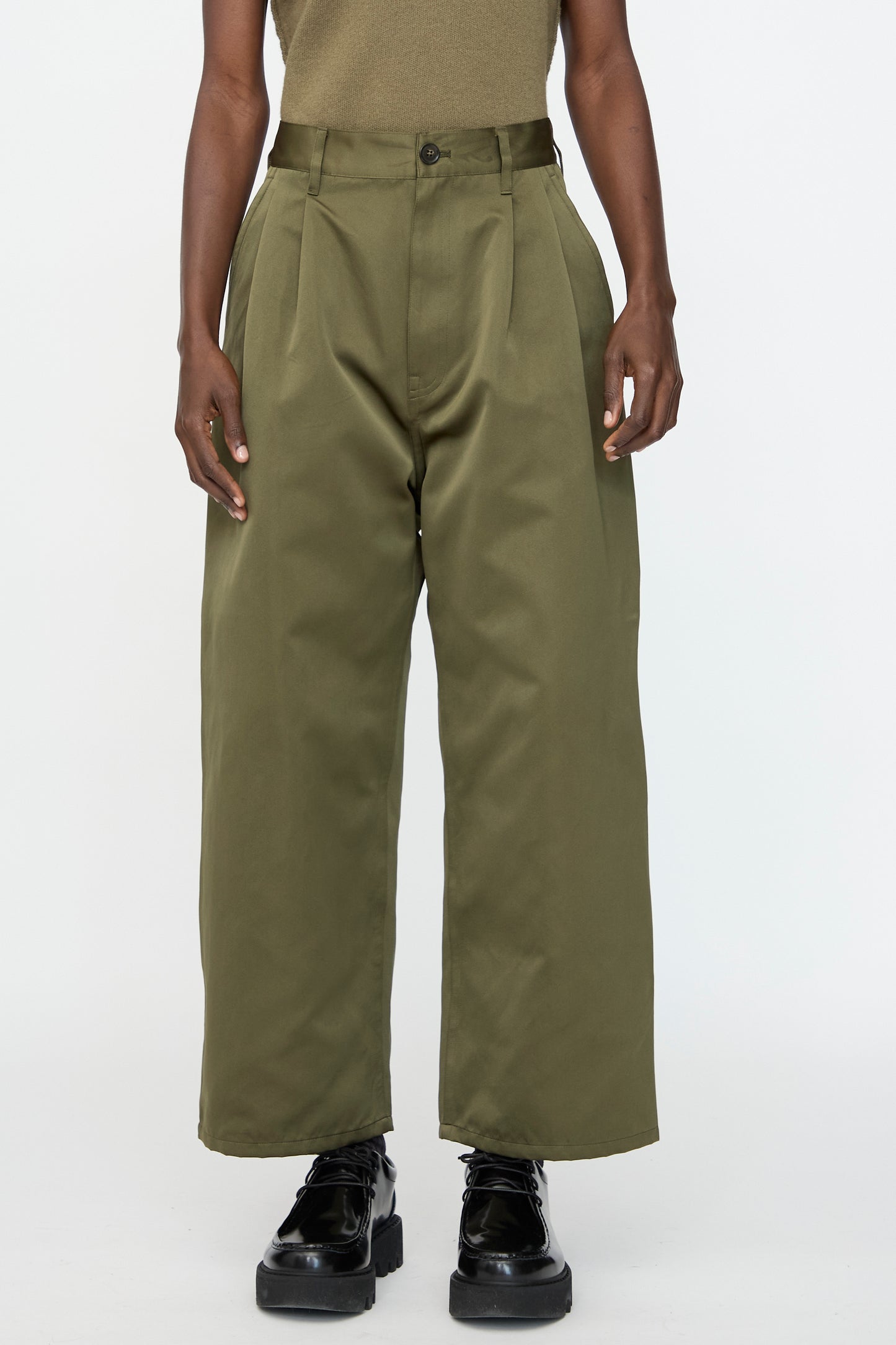 Wearing Sofie D'Hoore's Satin Polke Pant in Laurel, paired with black shoes and a khaki top, standing against a plain white background.