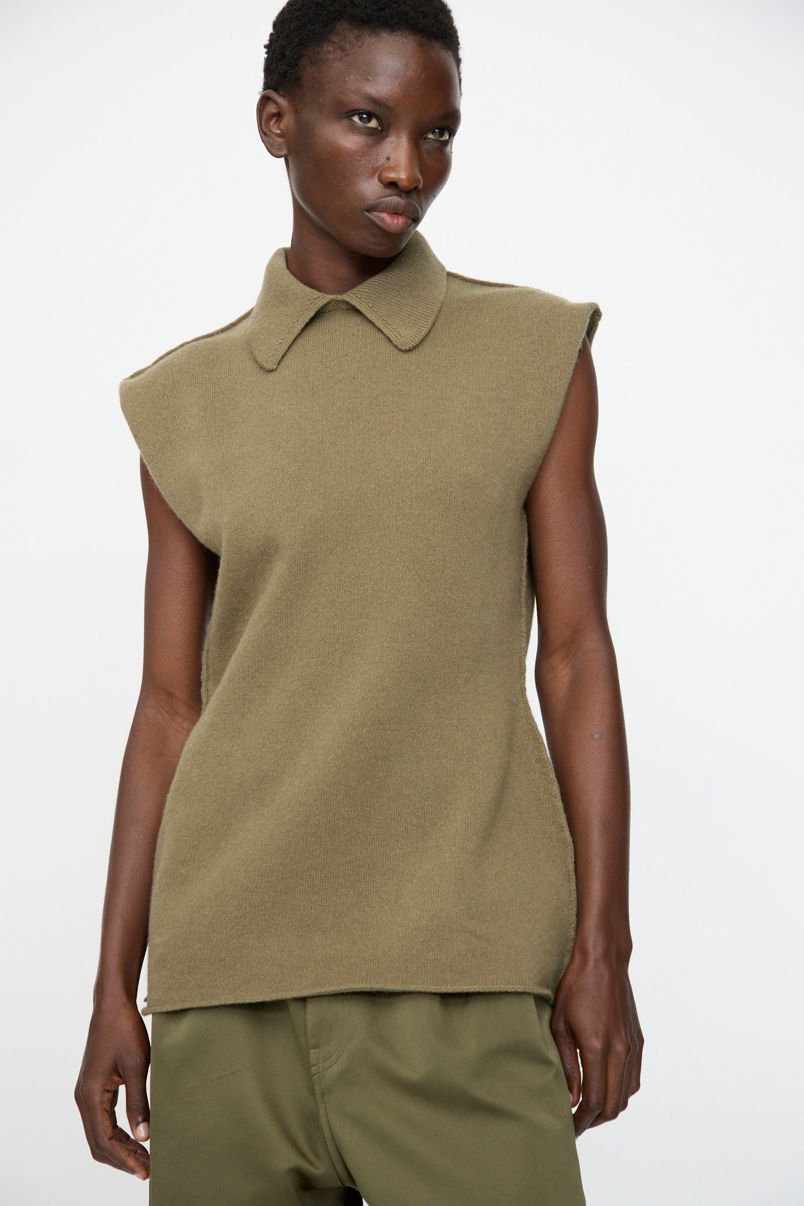 Model wears the Sofie D'Hoore Superfine Wool May Sleeveless Sweater in Sage with matching green pants, set against a plain white background.