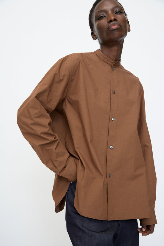 A person wears the Sofie D'Hoore Washed Poplin Braque Shirt in Chestnut with dark trousers, standing against a plain white background.