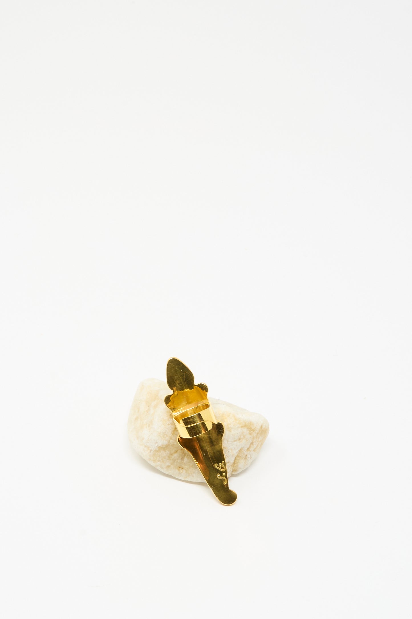 The Alligator Ring in Yellow by Sofio Gongli gleams on a light stone, its gold-plated surface shining like a hair clip, set against a plain white background.