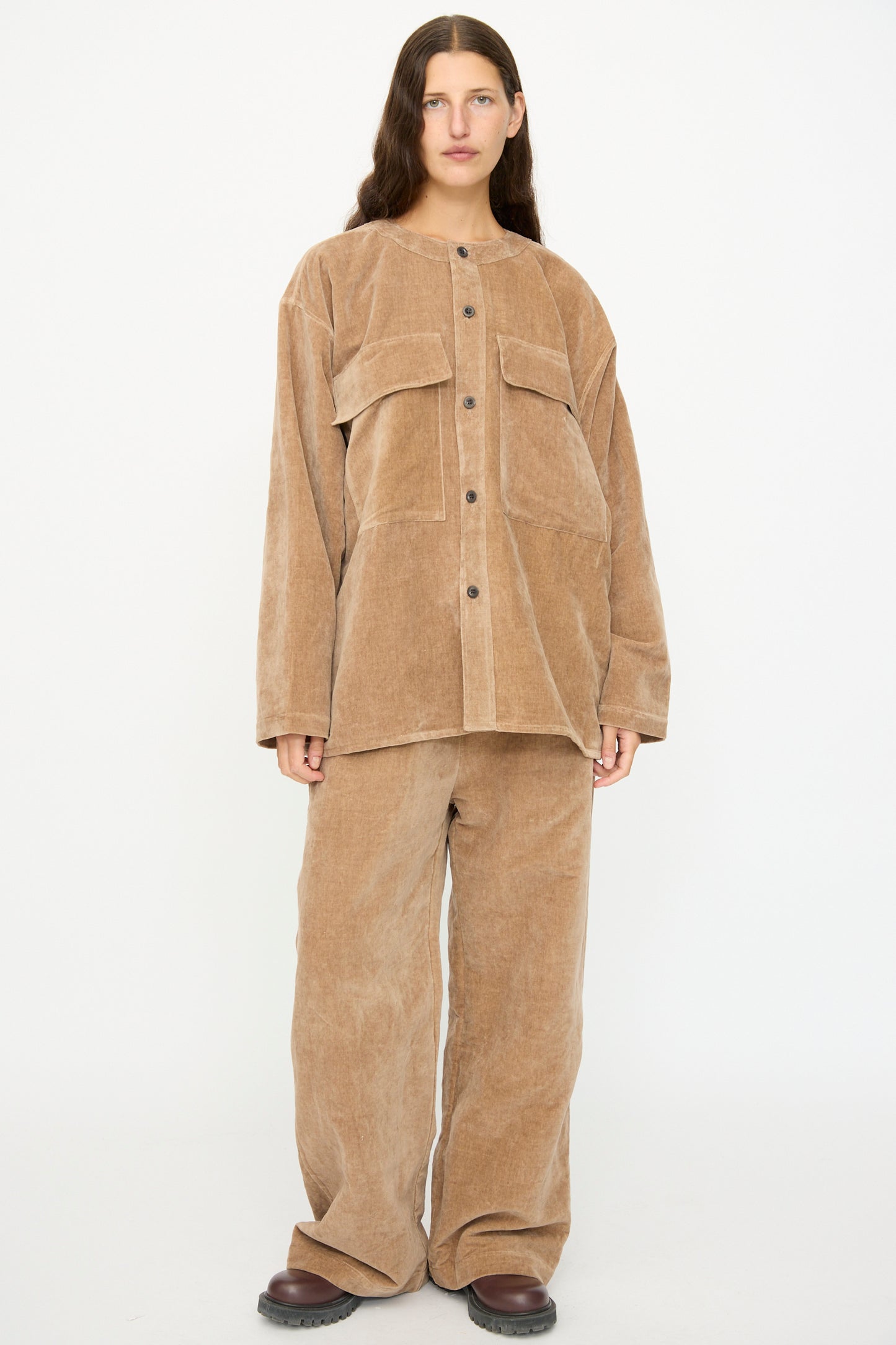 A person stands against a white background wearing the SONO Sid Shirt in Desert Rose, a relaxed fit corduroy button down with large front pockets, paired with matching wide-leg pants.