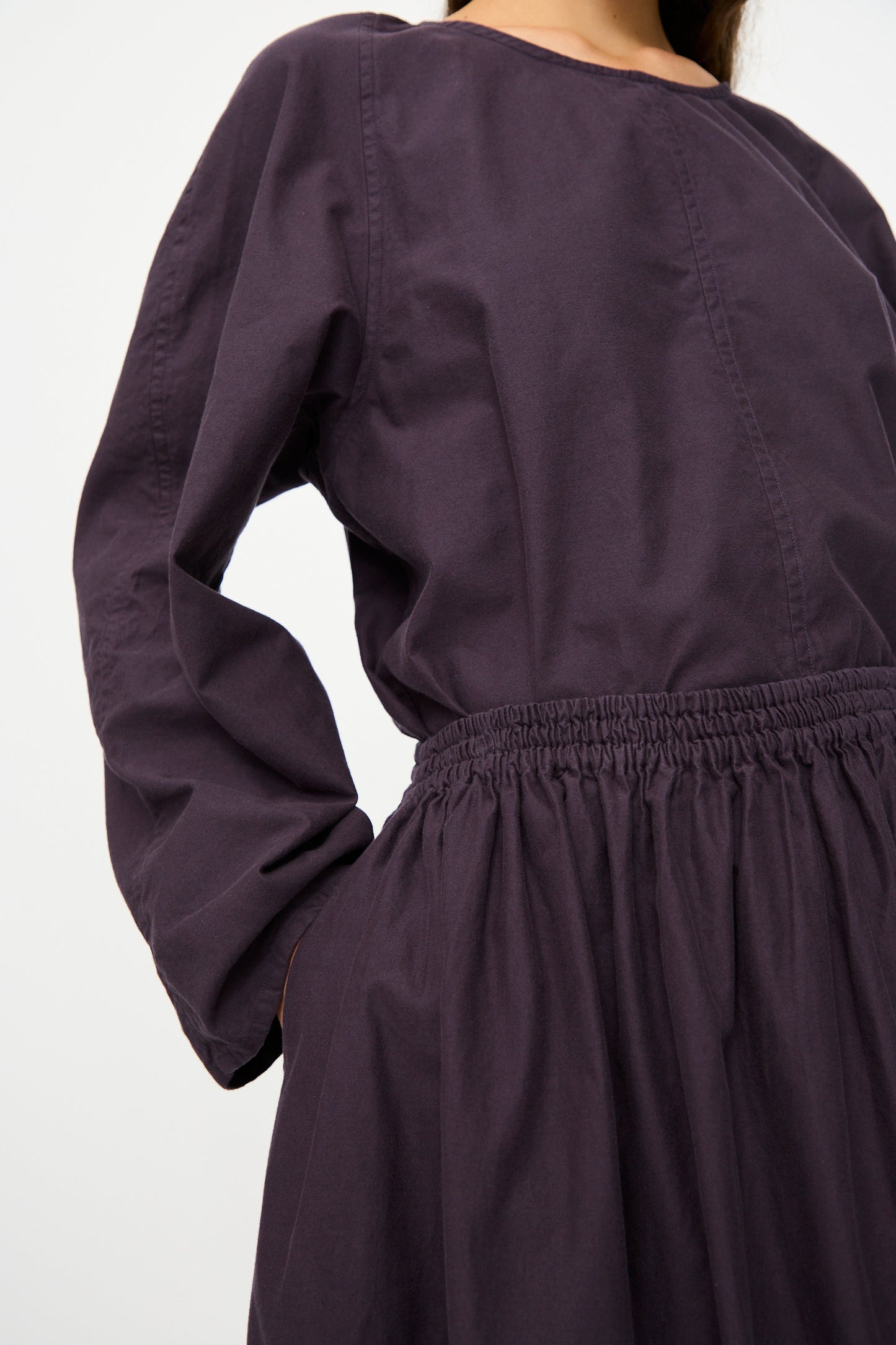 A person wearing the SONO Skye Skirt in Dark Grape, a loose-fitting, organic cotton skirt with an elastic waistband and a flowing silhouette, photographed from mid-chest to mid-thigh.