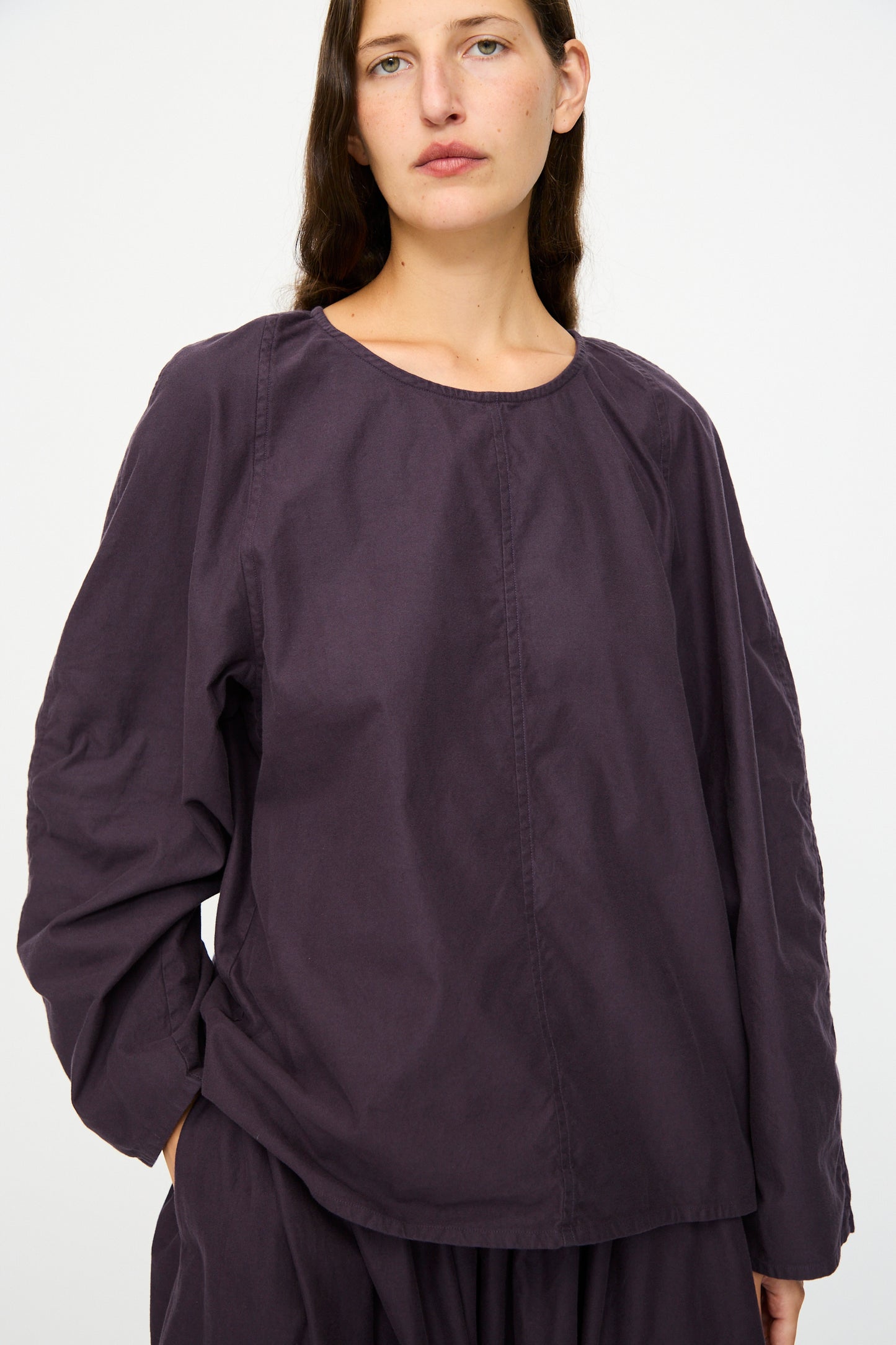 A person with long brown hair wears the SONO Tiga Top in Dark Grape, paired with matching pants, standing against a plain light background.