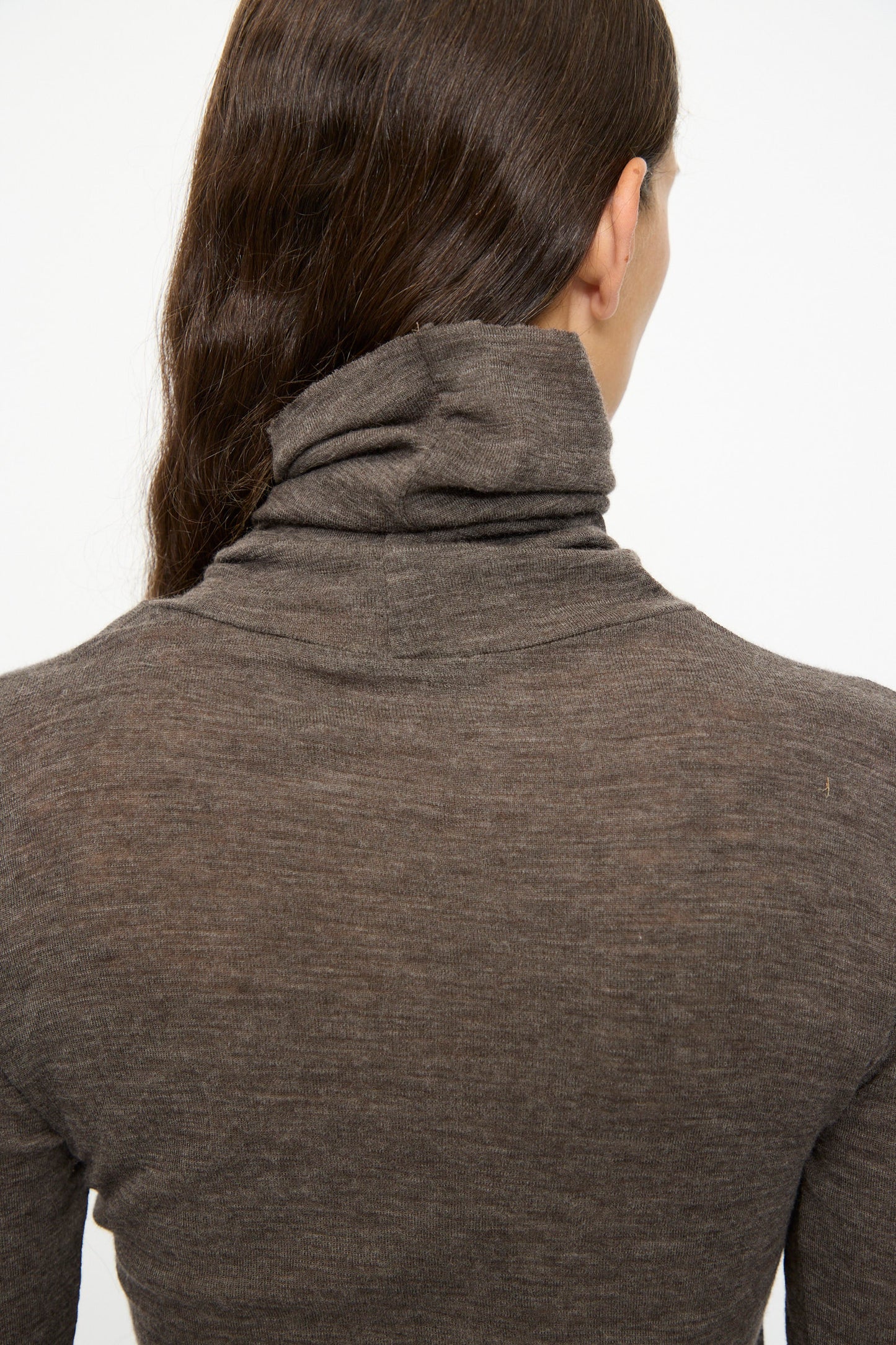 A person with long brown hair, shown from the back against a plain white background, wears the SONO Wool Roberta Rollneck in Charcoal.