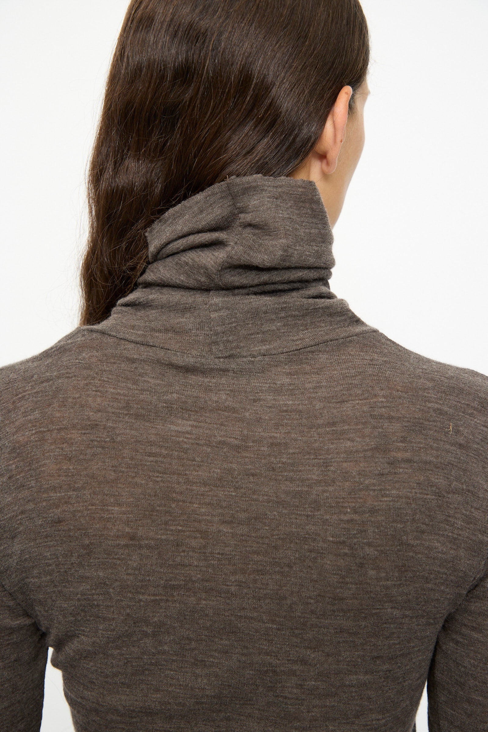 A person with long brown hair, shown from the back against a plain white background, wears the SONO Wool Roberta Rollneck in Charcoal.