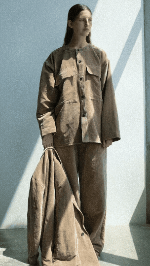 A woman putting on a tan blazer wearing a tan top and bottom.