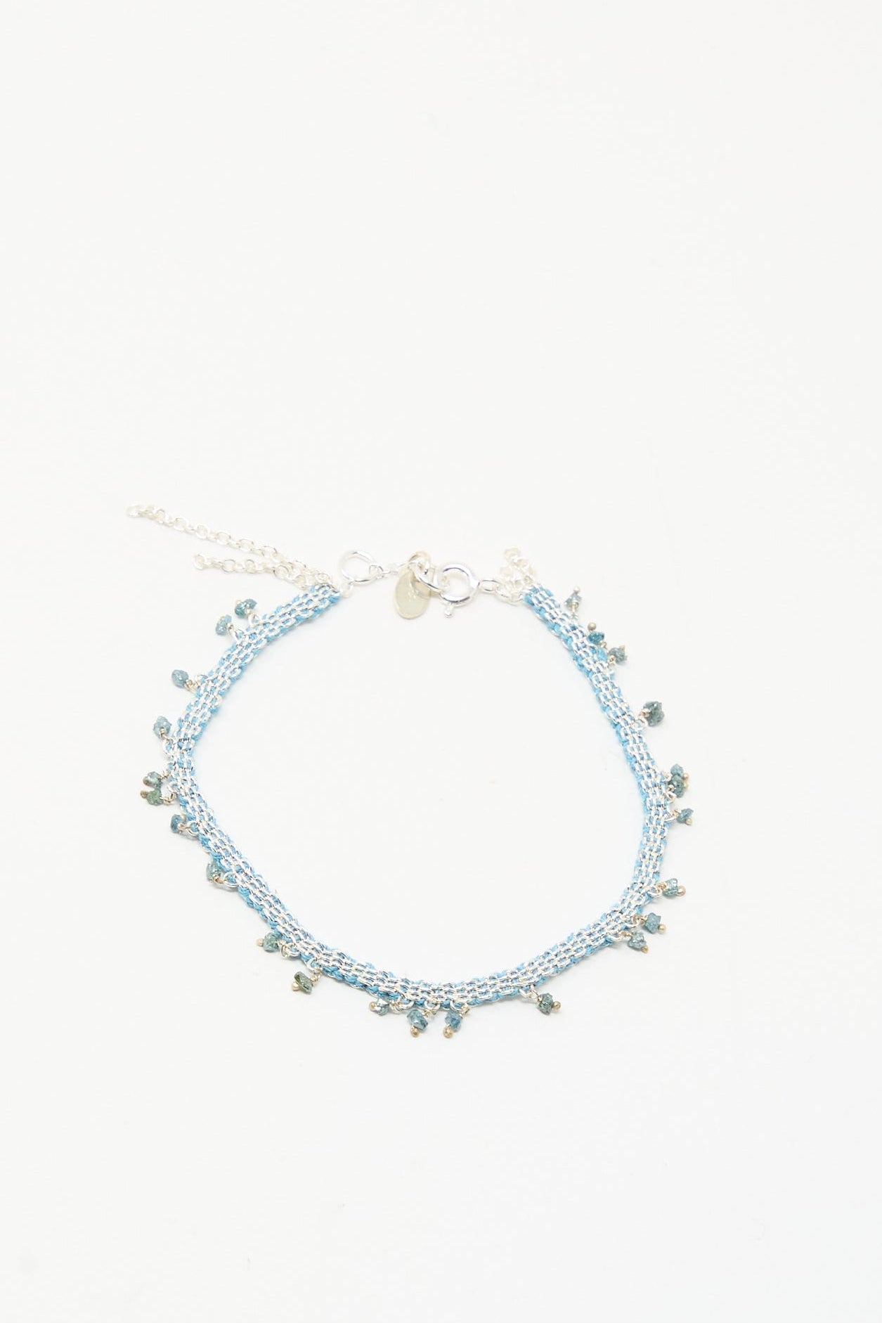 The Stephanie Schneider Silver and Silk Bracelet with Raw Blue Diamonds features delicate light blue silk, accented with raw blue diamonds and a silver clasp, displayed on a plain white background.