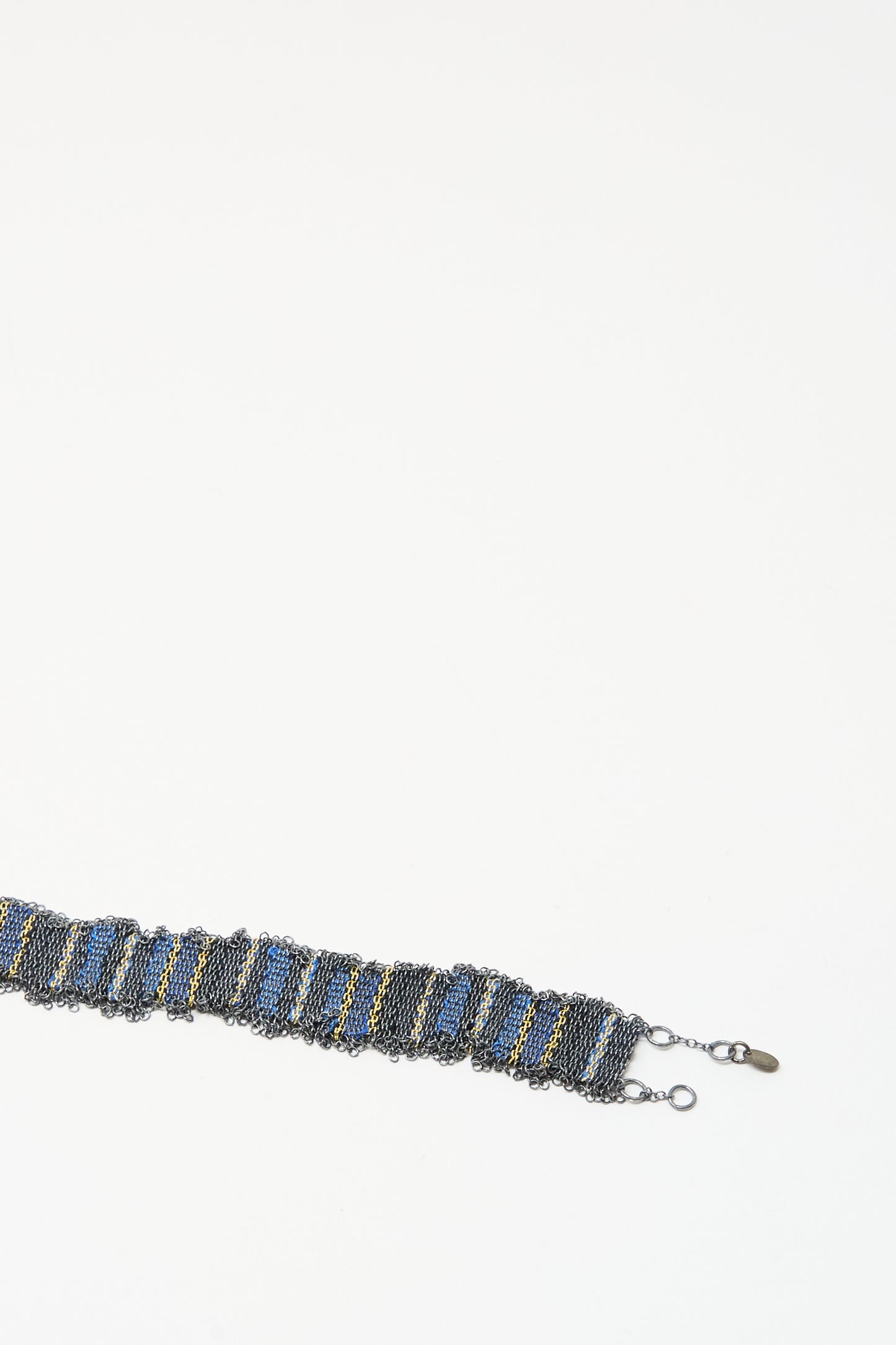 The Stephanie Schneider Silver and Silk Woven Bracelet in Blue features a wide graphic chain with blue and yellow accents and a clasp, shown on a white background.
