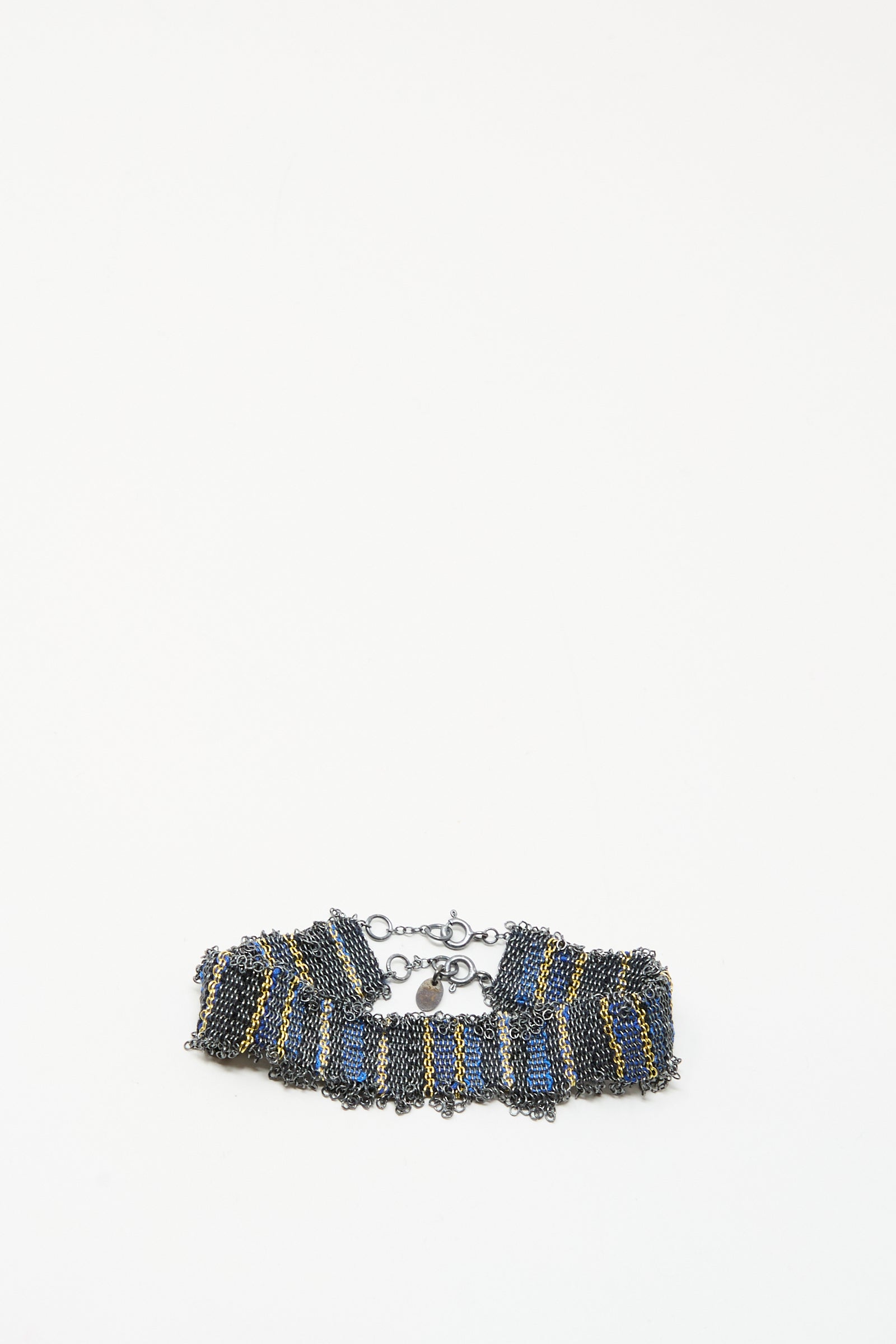The Silver and Silk Woven Bracelet in Blue by Stephanie Schneider showcases a ruffled design with blue, gold, and dark metallic chains, finished with a lobster clasp, set against a plain white background.