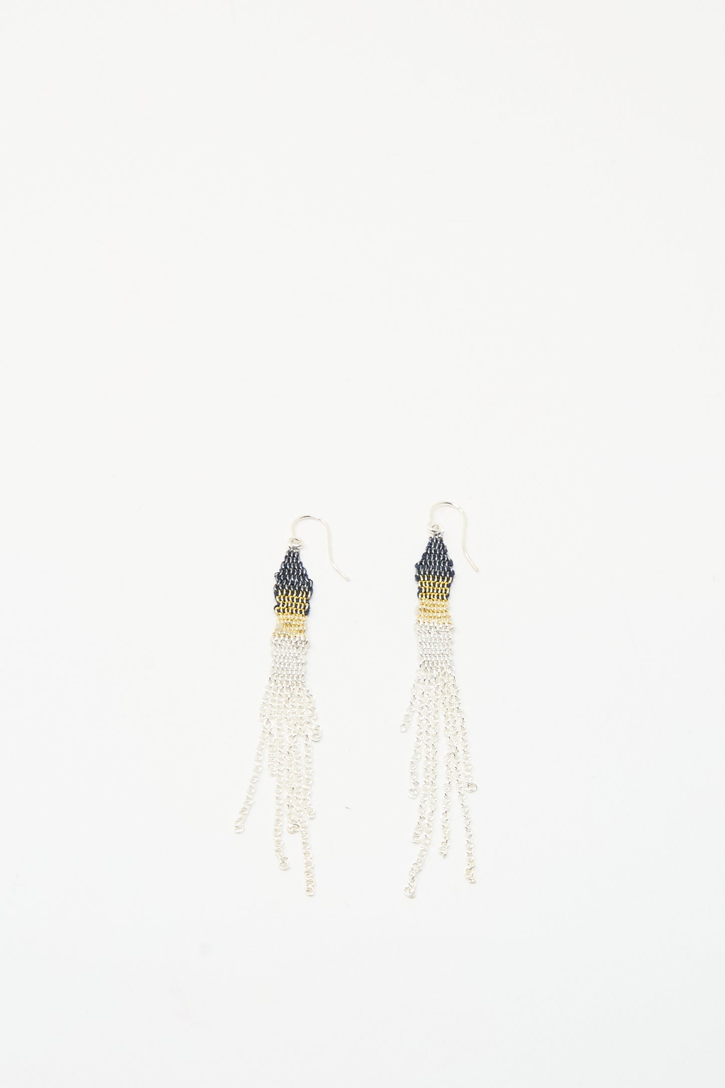 The Stephanie Schneider Silver and Silk Woven Earrings feature dark tops, gold accents, and multiple white silk thread strands, creating a beaded dangle look against a white background.
