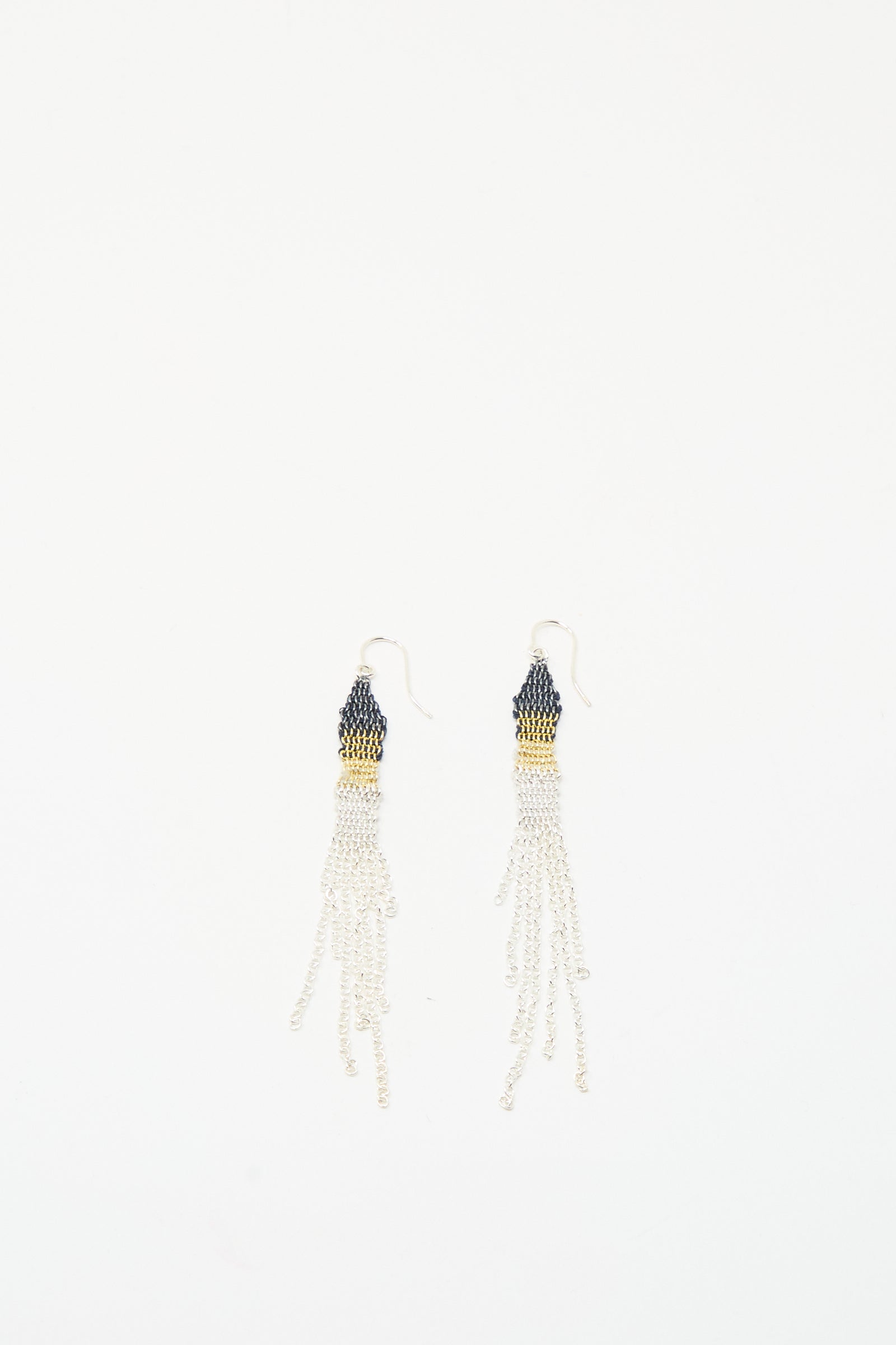 The Stephanie Schneider Silver and Silk Woven Earrings feature dark tops, gold accents, and multiple white silk thread strands, creating a beaded dangle look against a white background.
