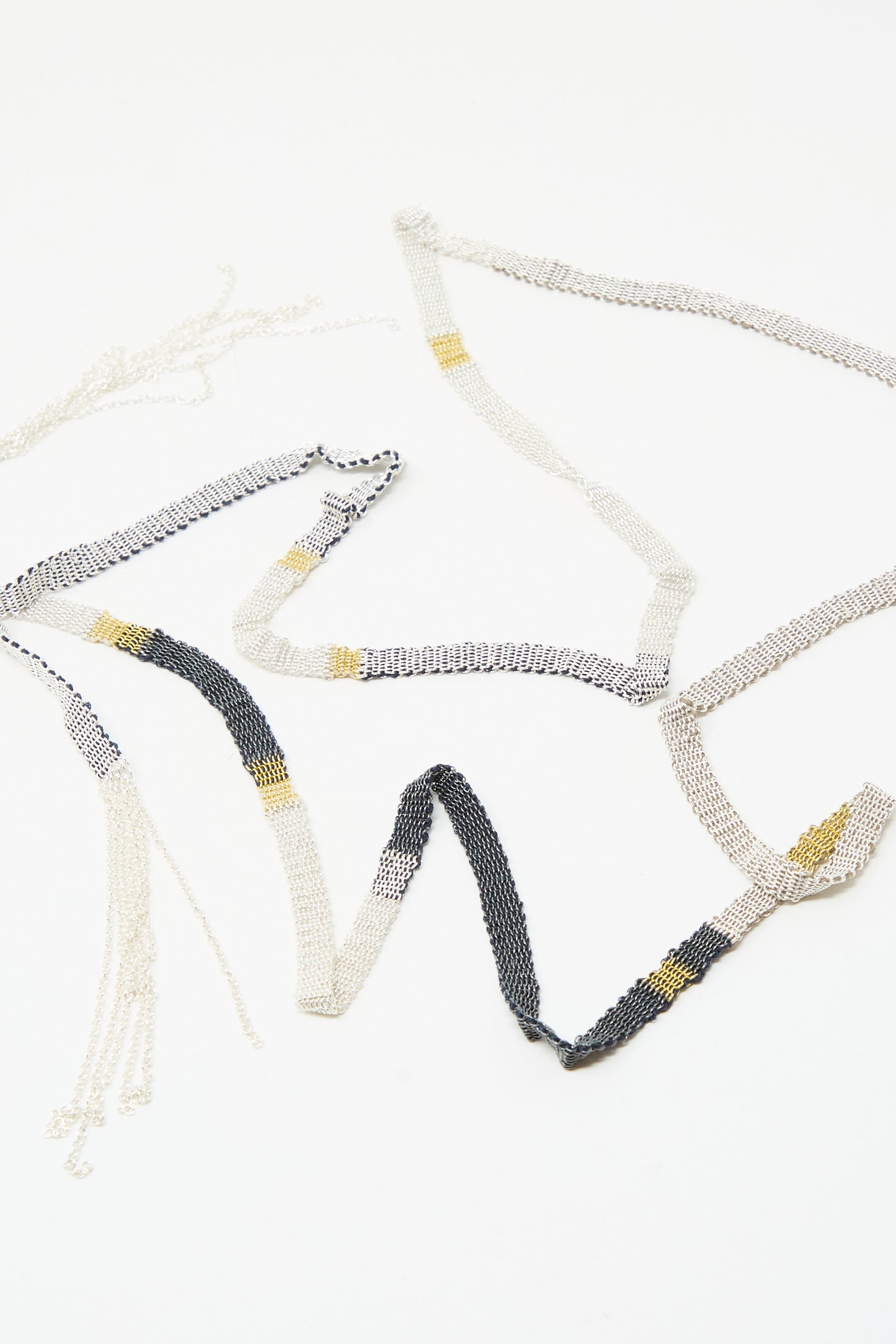 The Stephanie Schneider Silver and Silk Woven Shawl Necklace features alternating sterling silver, black, and gold links, artfully displayed on a white background.