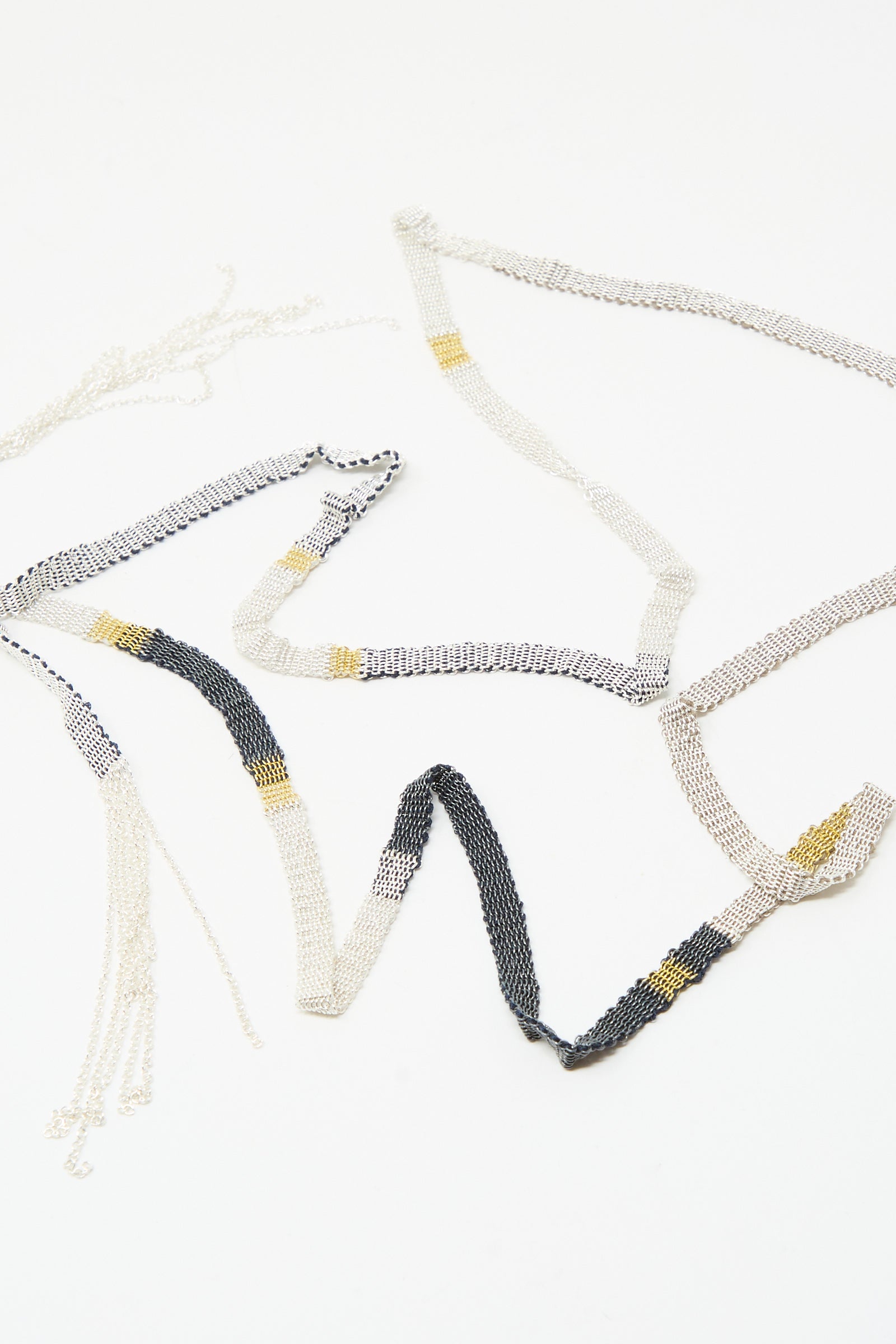 The Stephanie Schneider Silver and Silk Woven Shawl Necklace features alternating sterling silver, black, and gold links, artfully displayed on a white background.