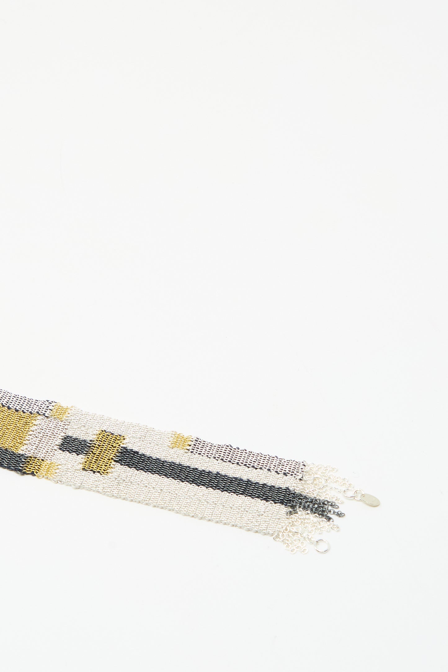 A close-up of the Stephanie Schneider Silver Oxidized, Gold Plated and Silk Woven Bracelet, featuring intricate patterns, displayed on a white background with empty space above.