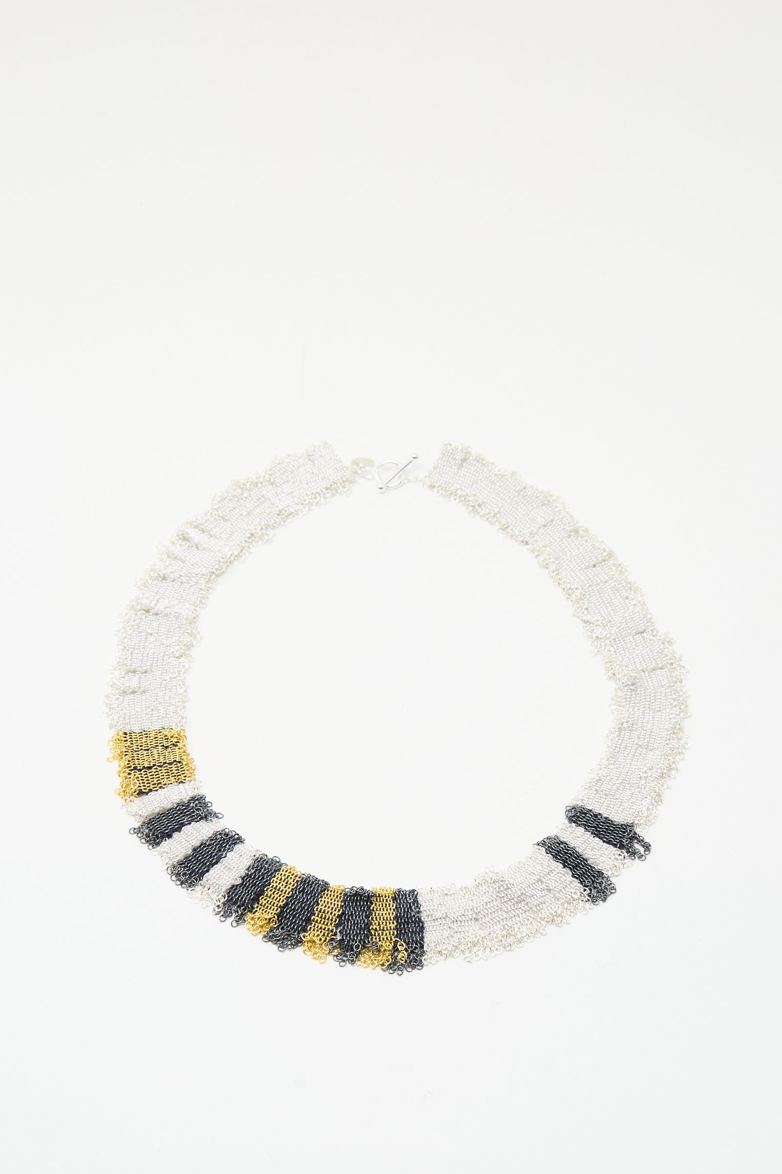 The Silver, Gold and Silk Woven Necklace by Stephanie Schneider features alternating white, black, and gold beads and a gold plated silver clasp, displayed against a plain white background.