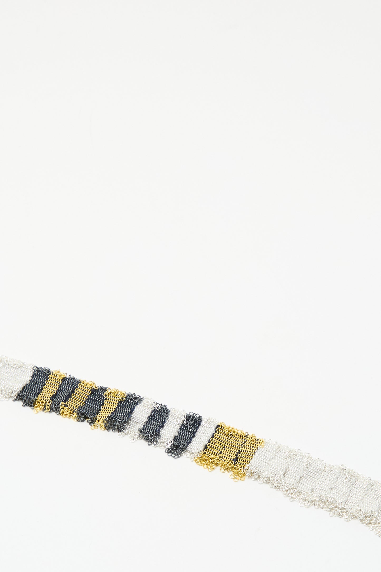 The Stephanie Schneider Silver, Gold and Silk Woven Necklace displays a striking pattern of alternating metallic and silk sections against a plain white background.