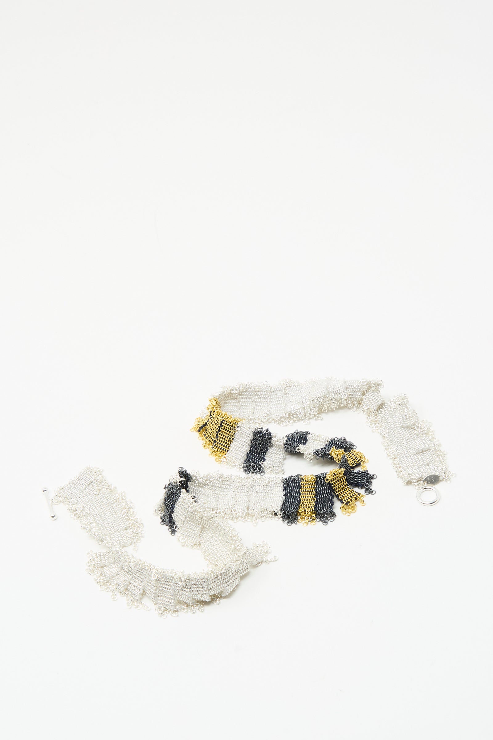 A beaded necklace in white, black, and gold segments, the Stephanie Schneider Silver, Gold and Silk Woven Necklace, displayed together on a plain white background.