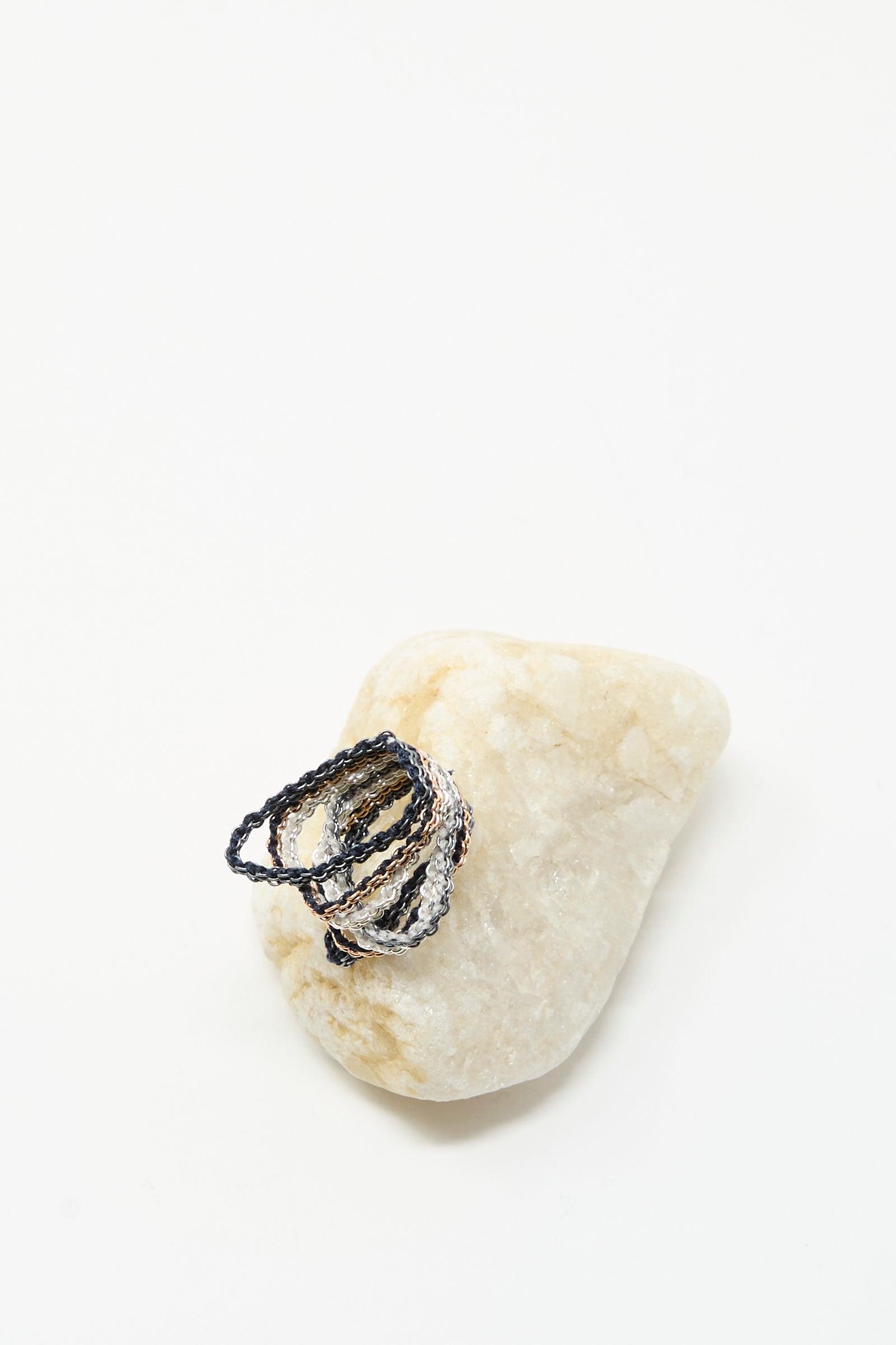 The Stephanie Schneider Silver, Rose Gold Plated and Silk Woven Ring is displayed atop a light-colored stone against a plain white background.