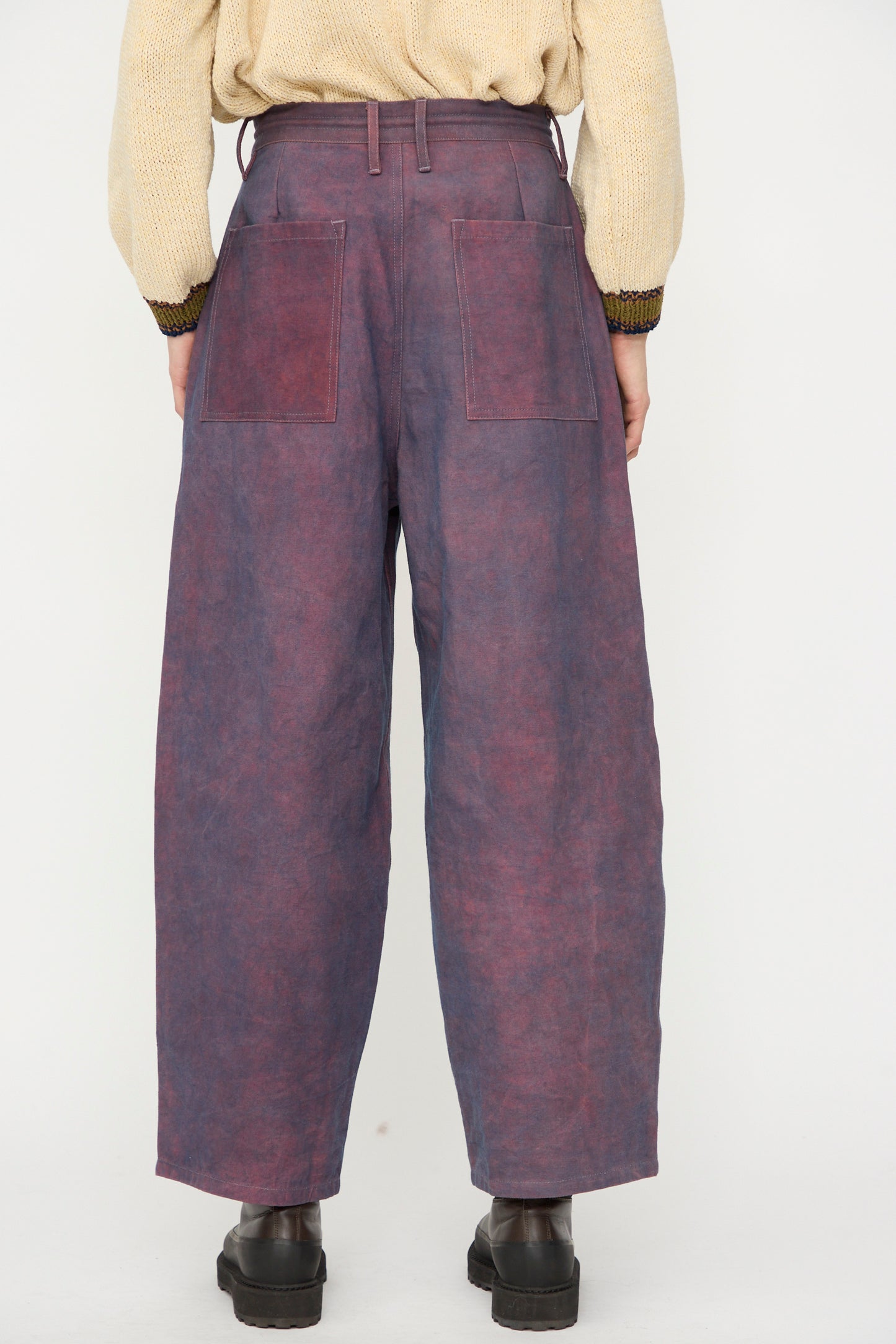 Person wearing the Story mfg. Canvas Document Pant in Ancient Purple—high-waisted, wide-leg trousers with large back pockets—paired with a beige sweater and black platform shoes, shown from the back.