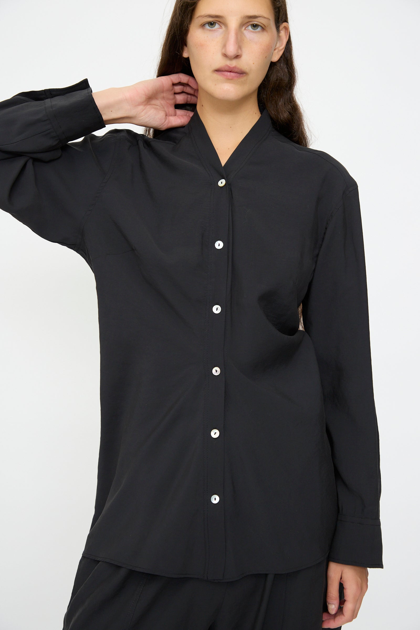 Model wears the Acre Top in Darkest Navy by Studio Nicholson, a loose-fit collarless button-up shirt with white buttons, against a plain white background.