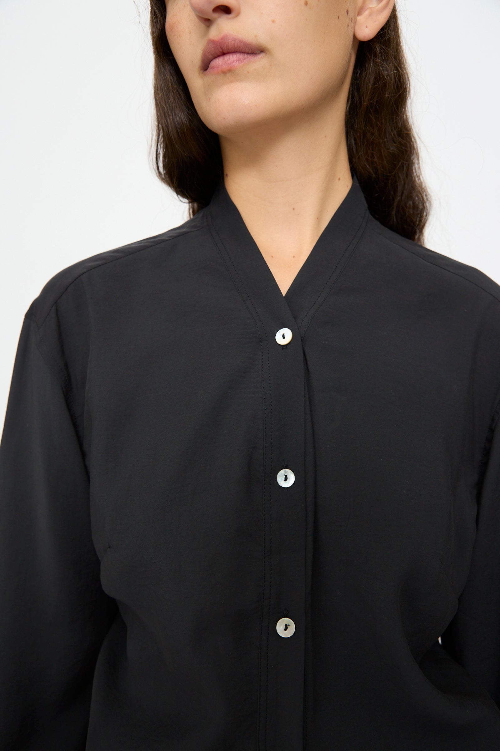 A person wearing the Studio Nicholson Acre Top in Darkest Navy, collarless and buttoned up, shown from the shoulders to just above the mouth.