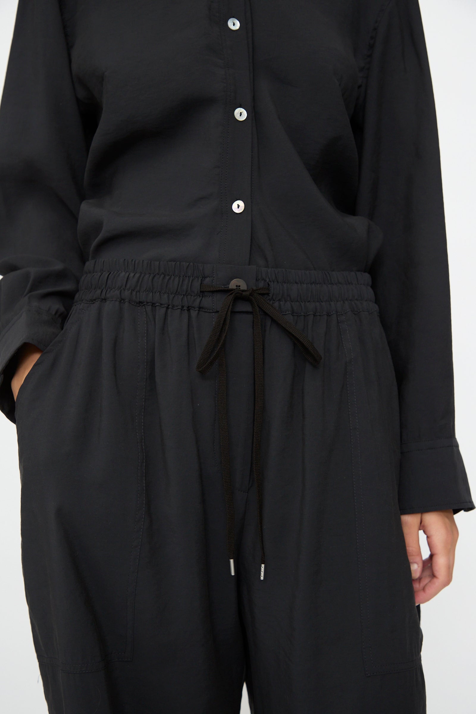 Person wears a black button-up shirt and Studio Nicholson Capel Pant in Darkest Navy, relaxed fit with drawstring waist, hands in pockets; shown from shoulders to mid-thigh.